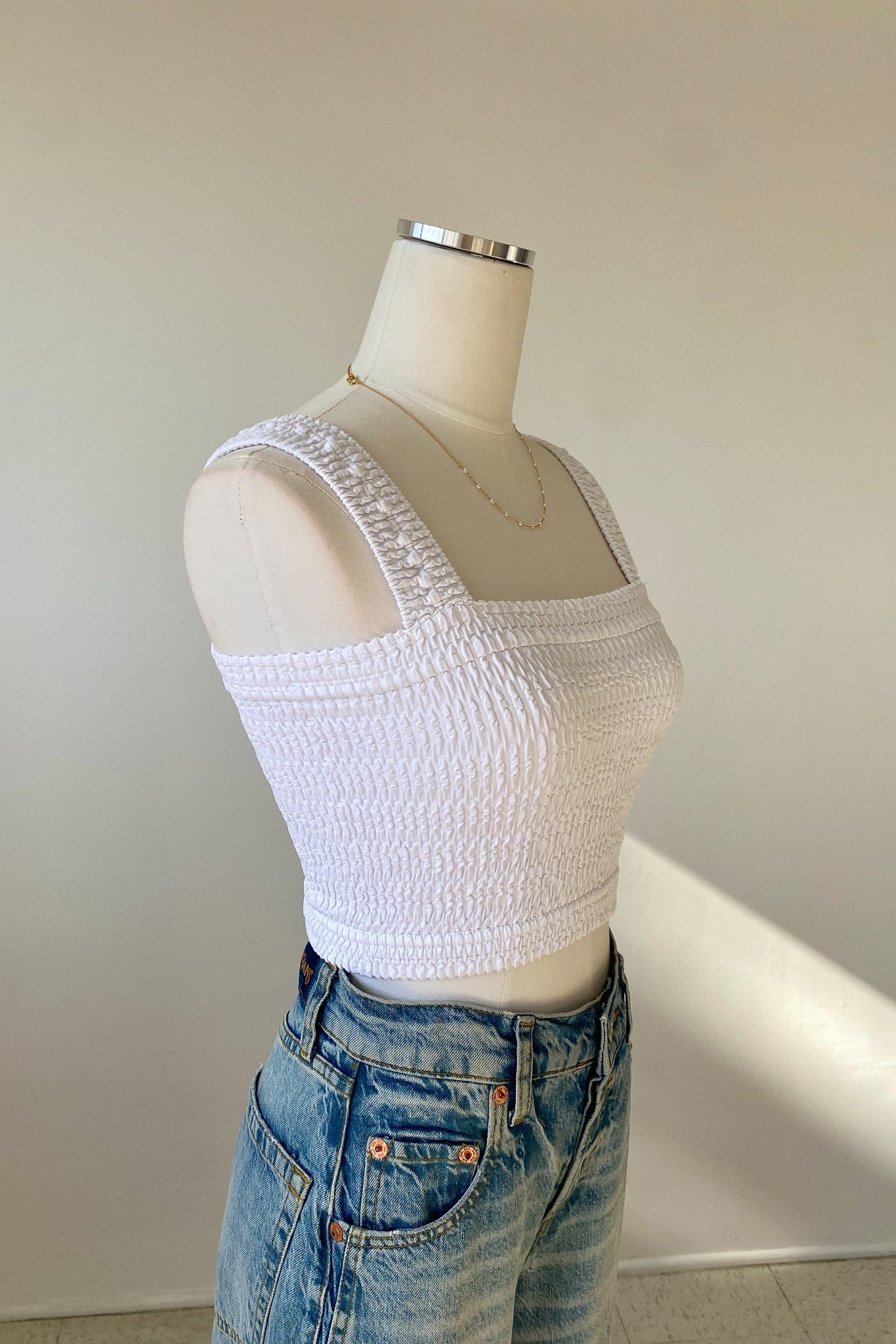 White textured crop top on a mannequin with blue jeans against a plain background