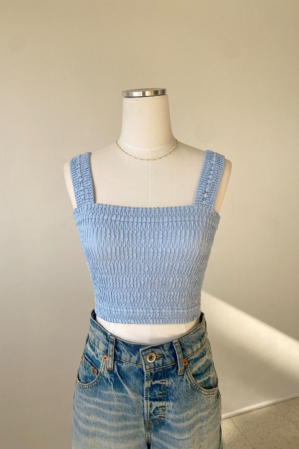 Mannequin wearing a light blue smocked top and high-waisted jeans against a plain background