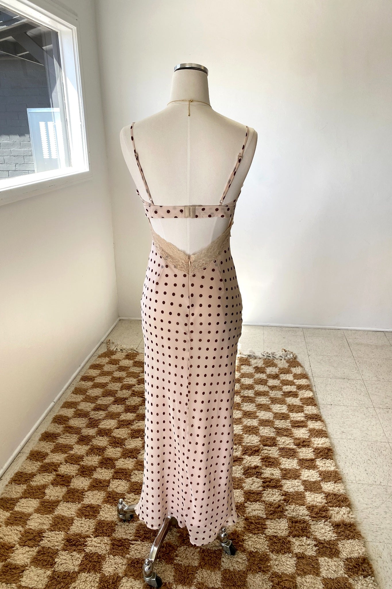 Mannequin wearing a polka dot dress on a checkered floor with a white wall background
