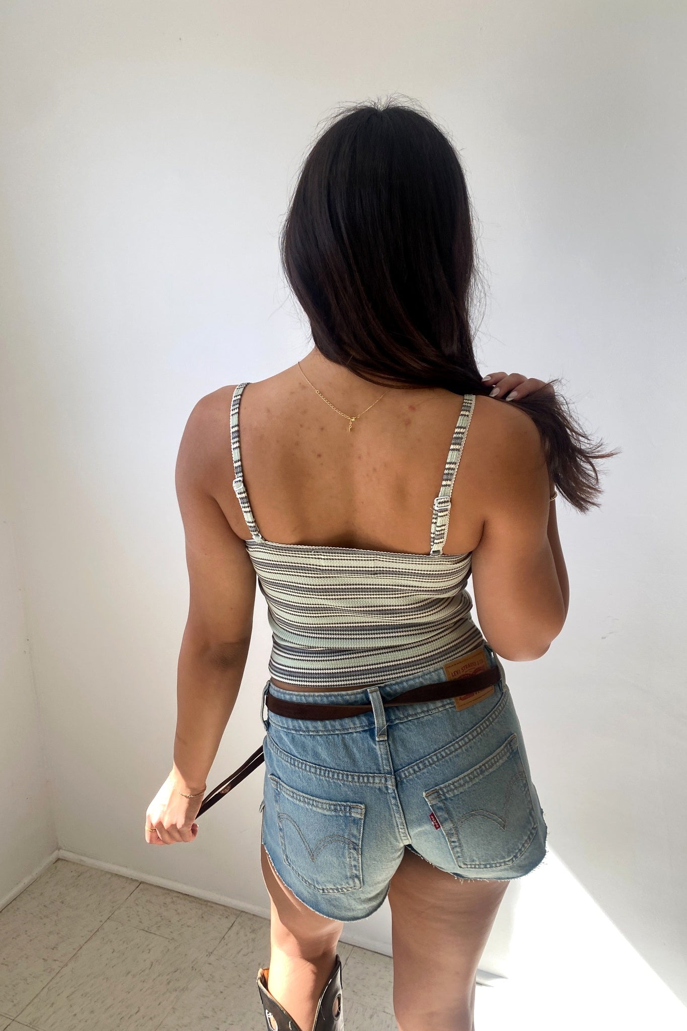 Person wearing a striped tank top and denim shorts against a white wall.