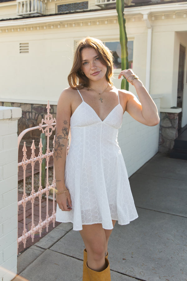 Woman in a white dress standing outdoors near a building with a pink gate.