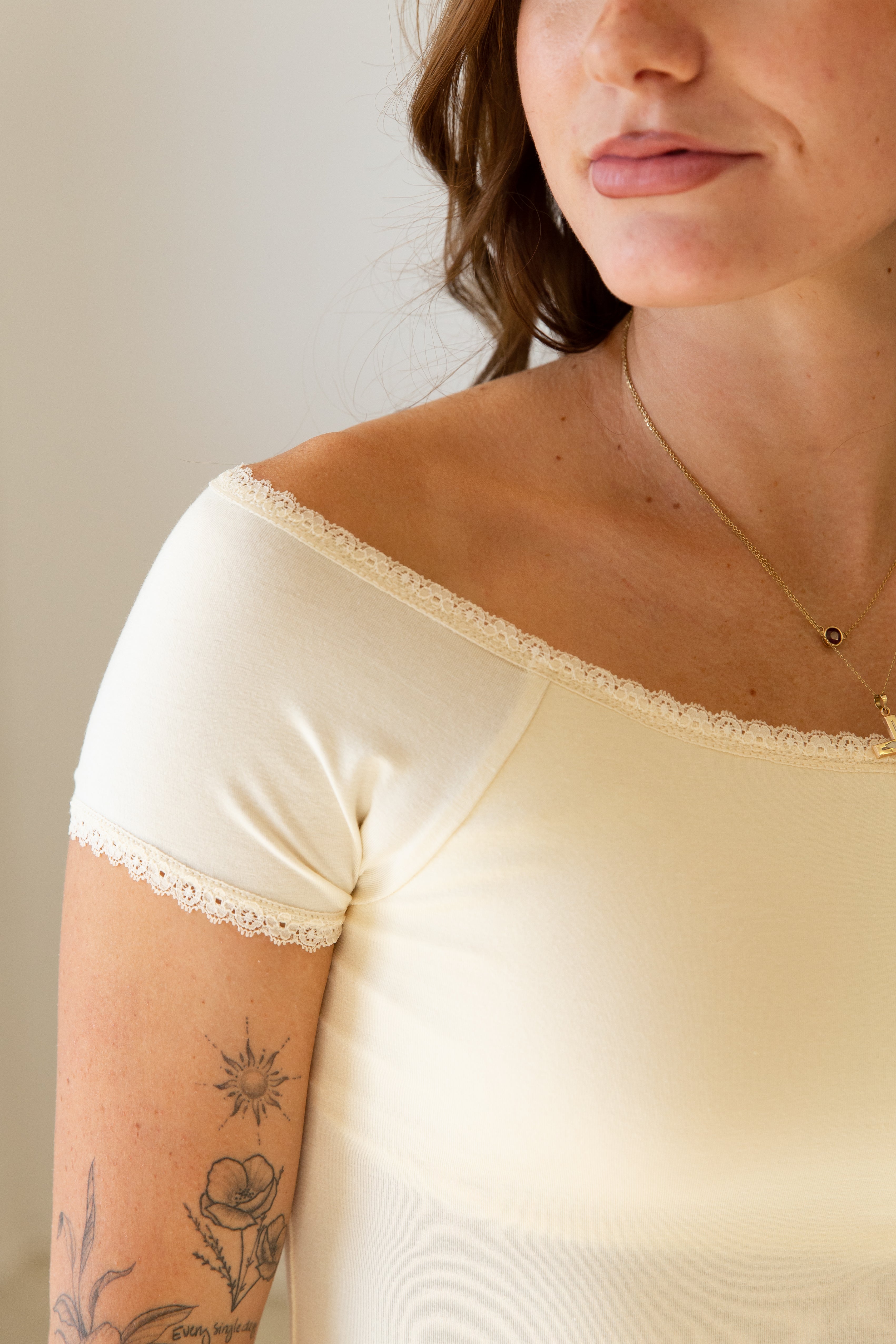 Woman wearing a beige lace-trimmed top against a neutral background