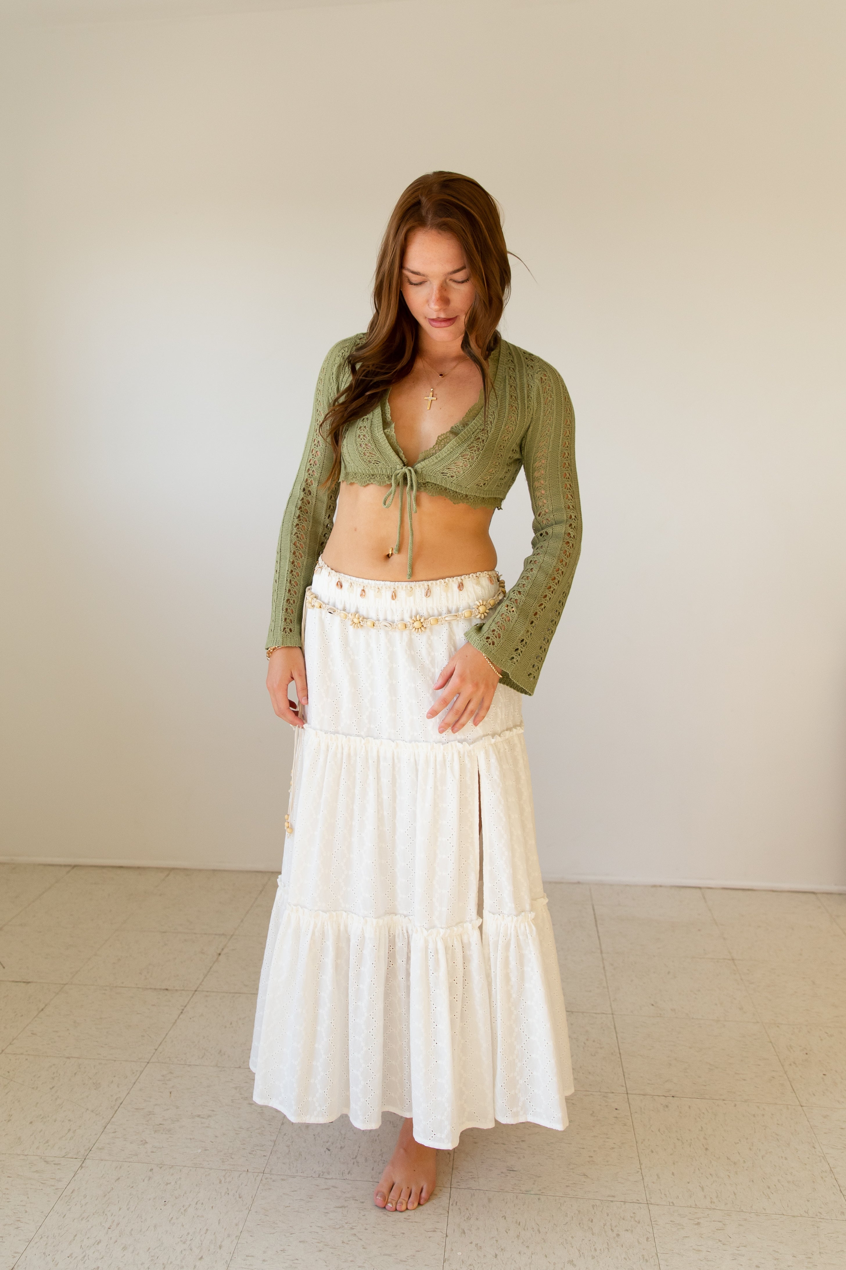 Woman wearing a green cardigan and white skirt against a plain background