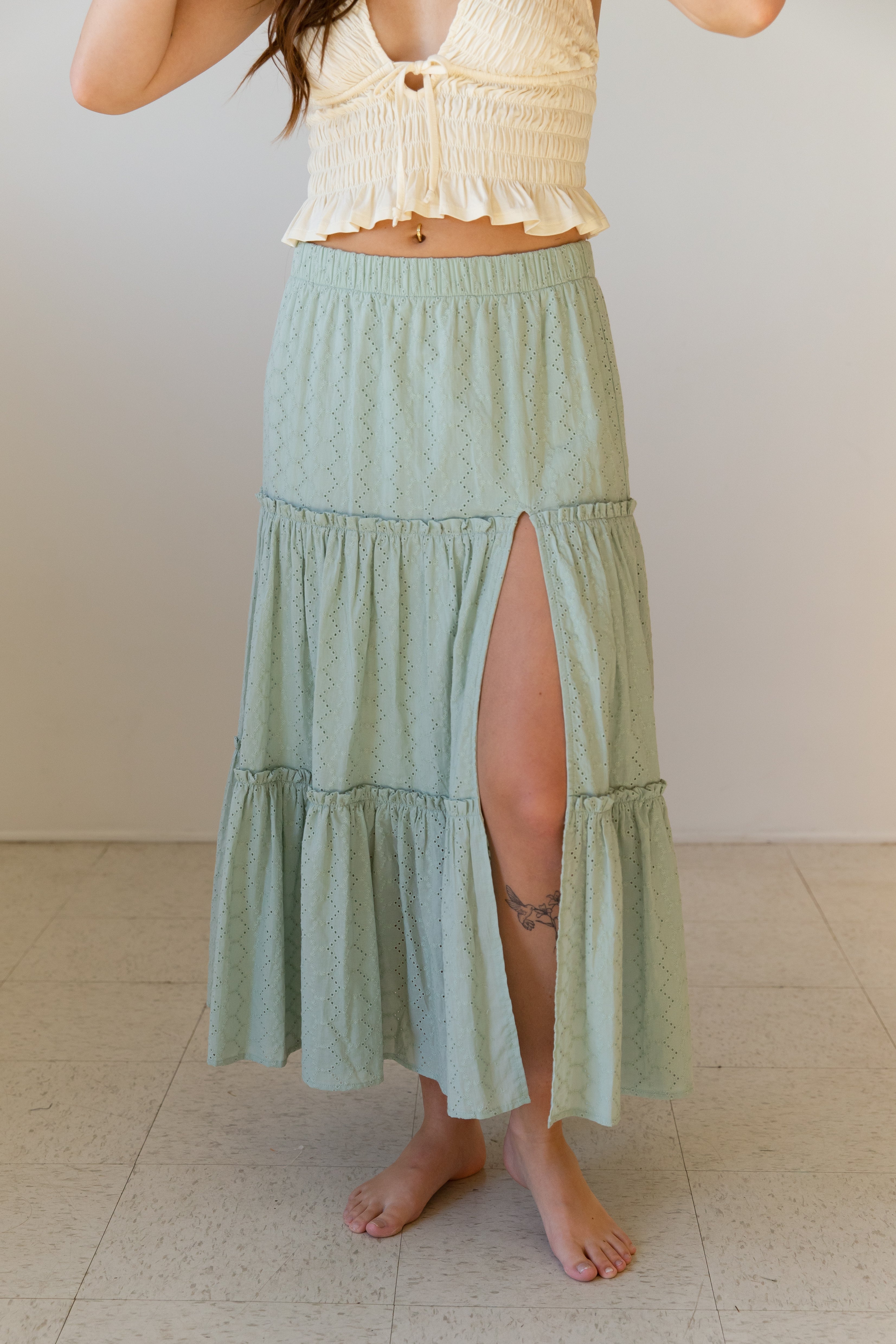 Person wearing a light green tiered skirt with a white top against a plain background