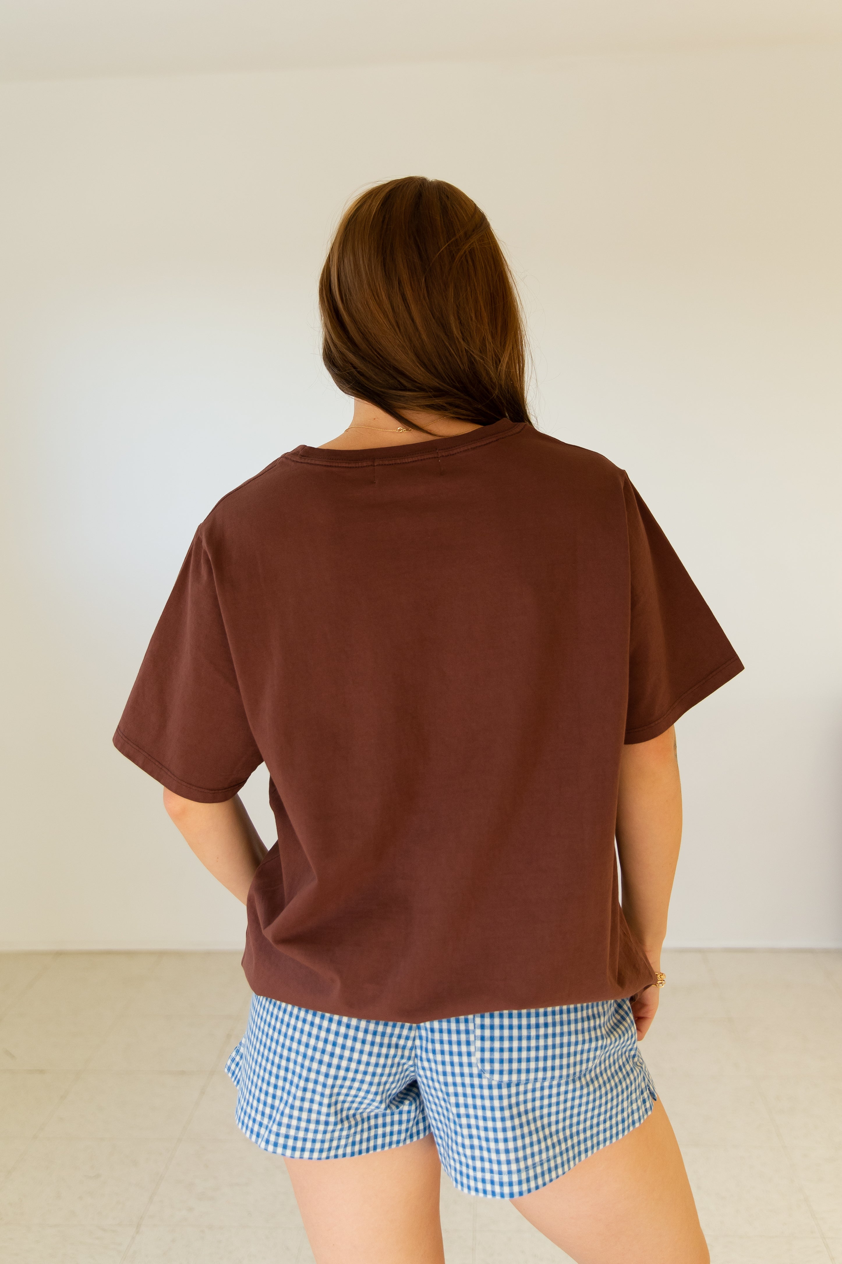 Person wearing a brown t-shirt and blue checkered shorts against a plain background