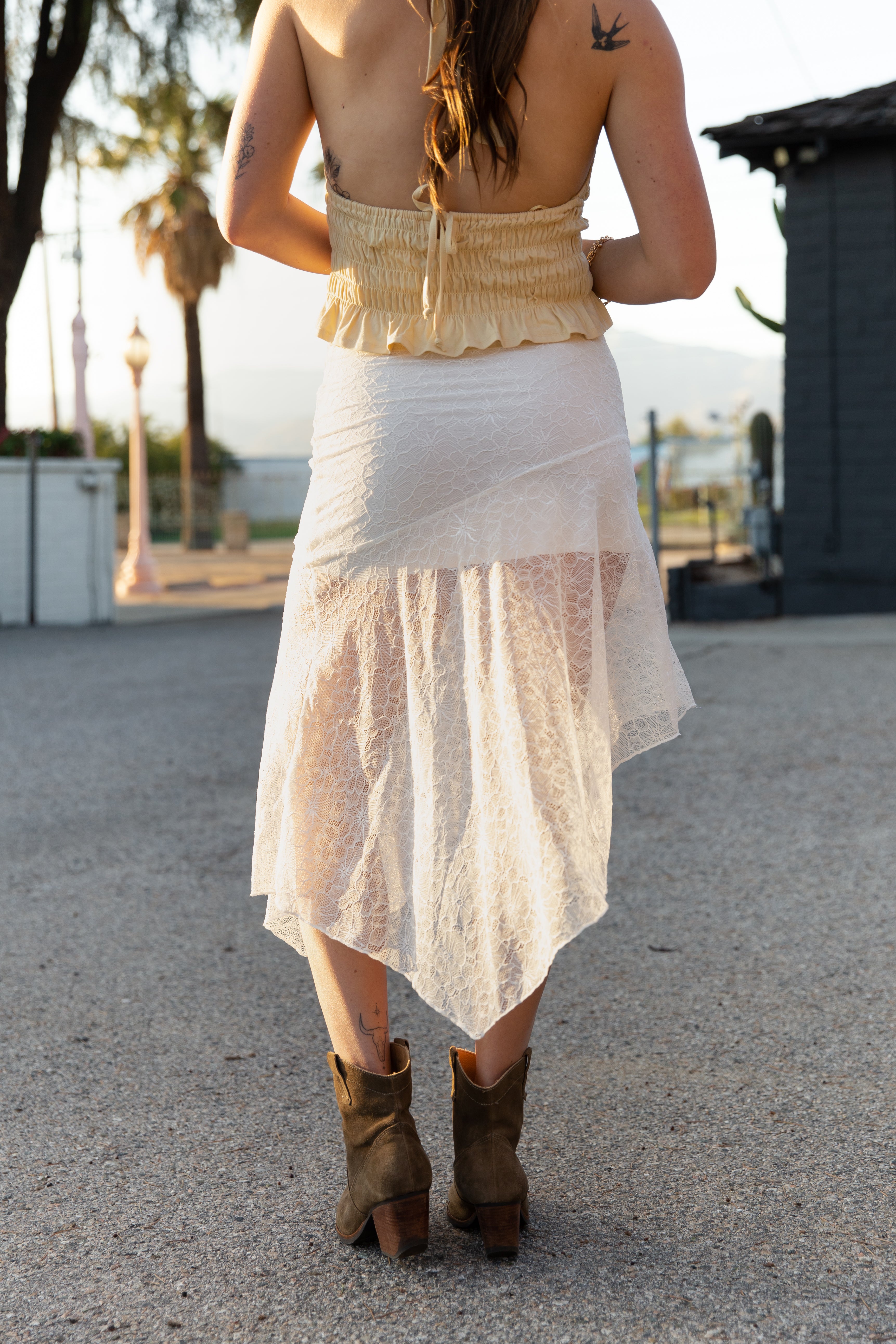 Person wearing a yellow top and white skirt with brown boots on a street.
