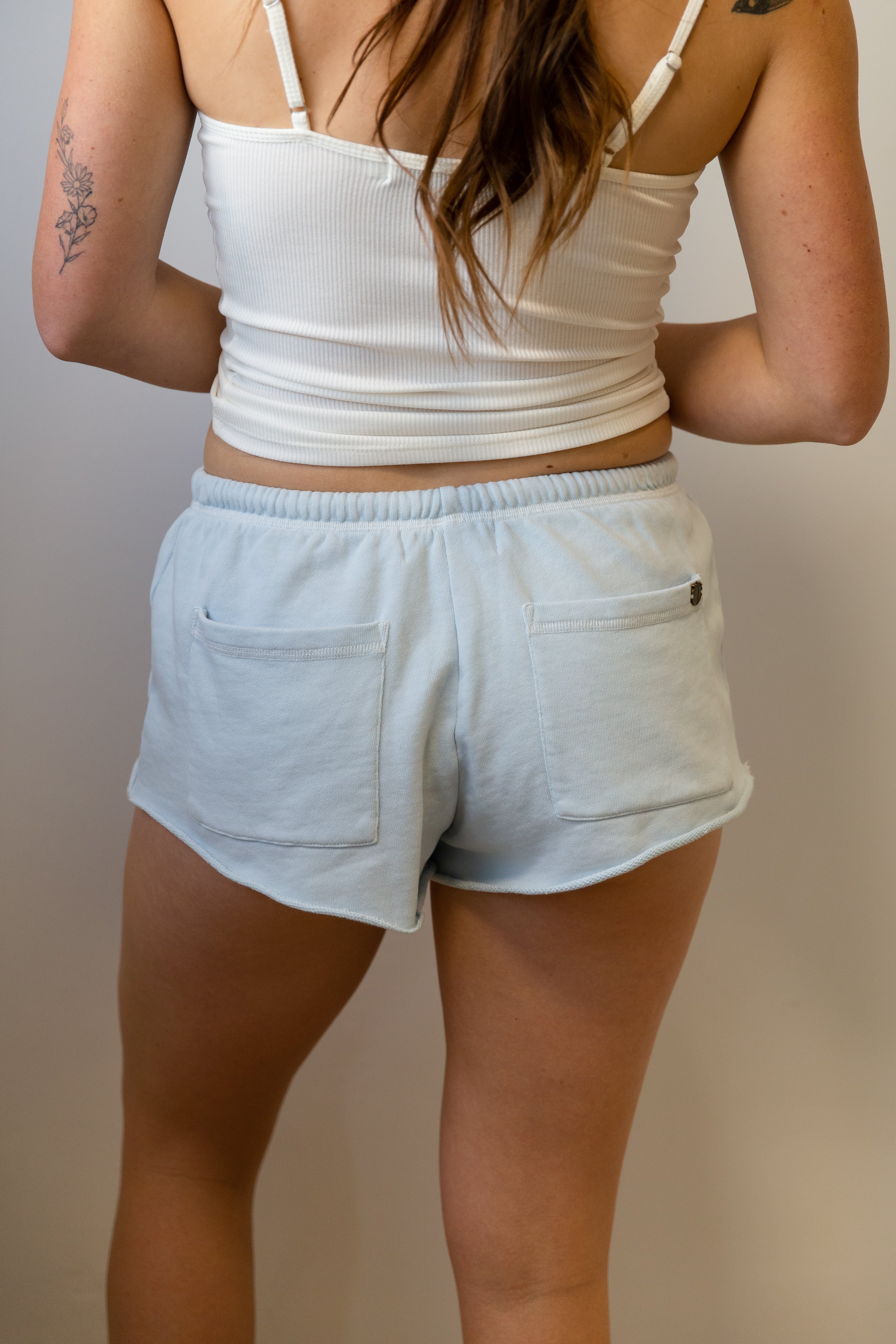 Person wearing a white tank top and light blue shorts against a neutral background