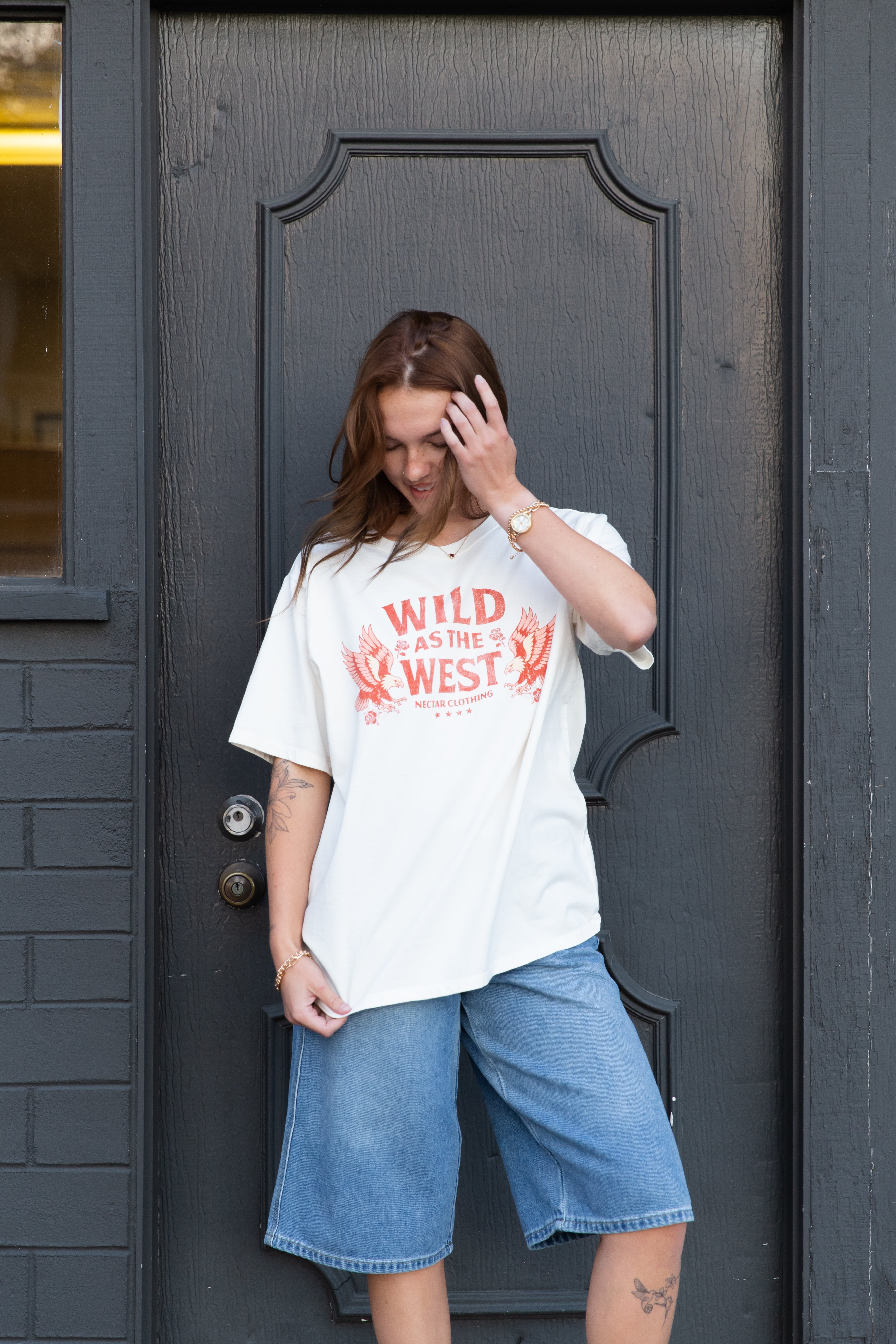Woman wearing a 'Wild West' t-shirt standing in front of a dark door.