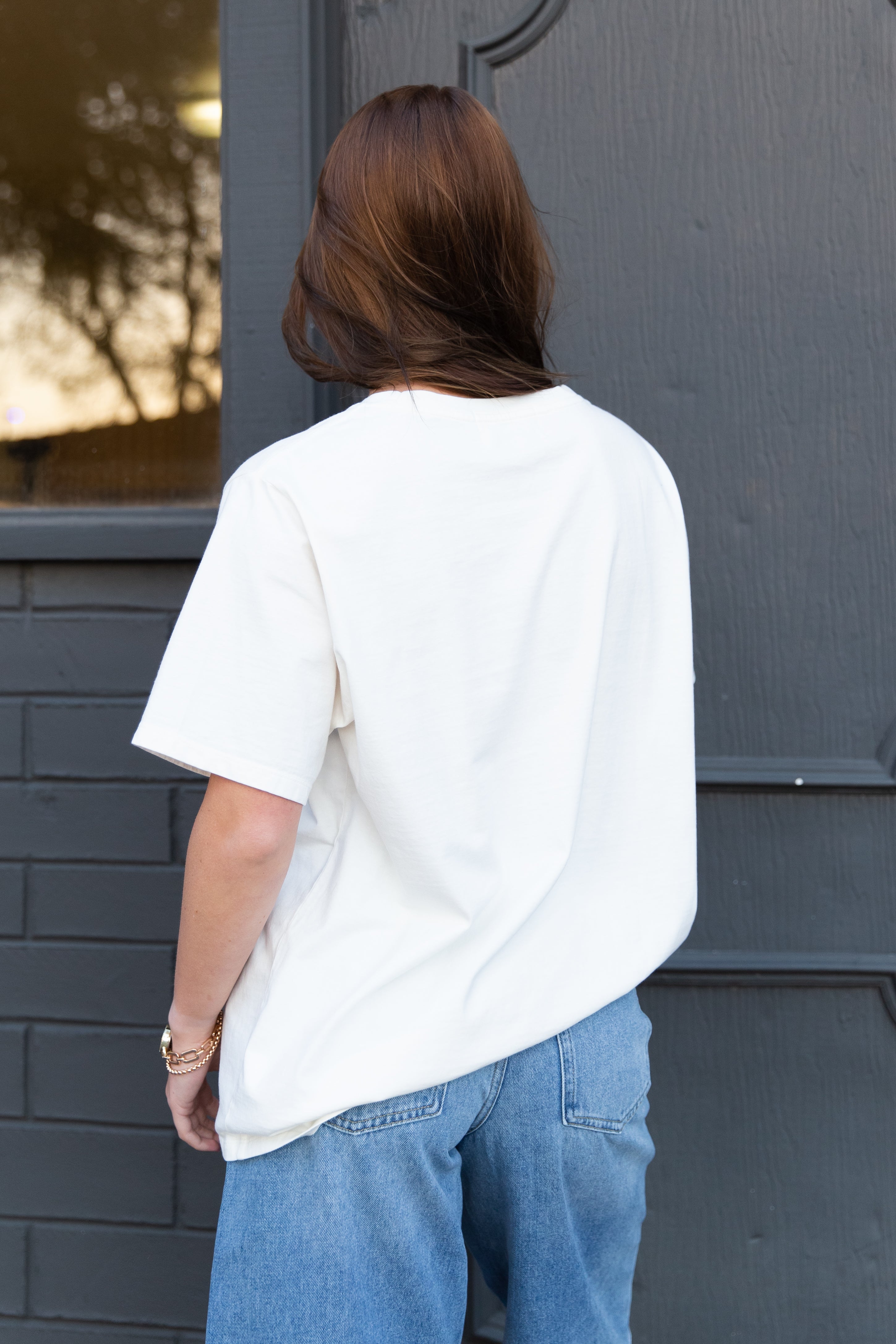 Person wearing a white t-shirt and blue jeans standing in front of a gray door.