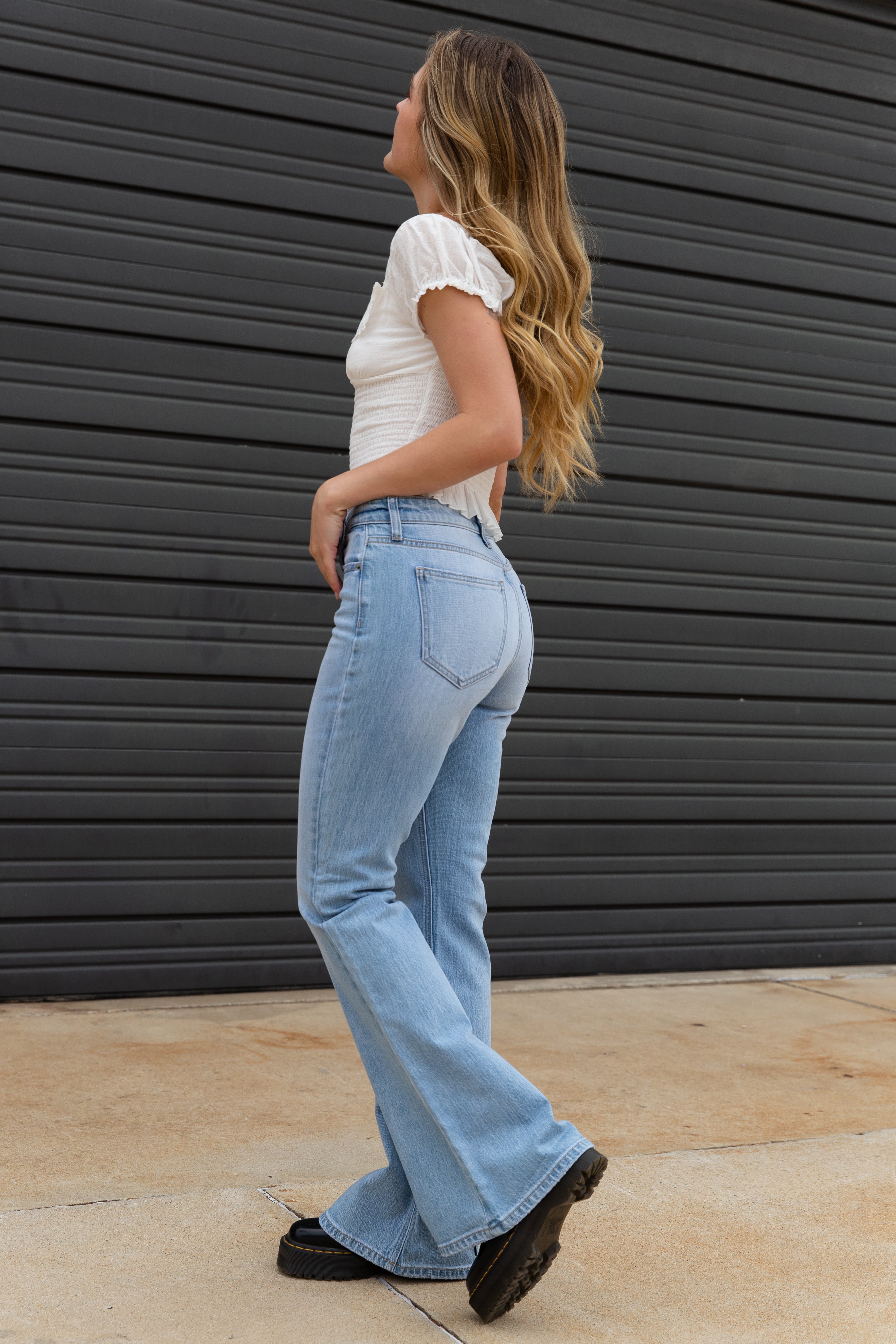 Woman wearing light blue jeans and a white top against a dark gray wall.