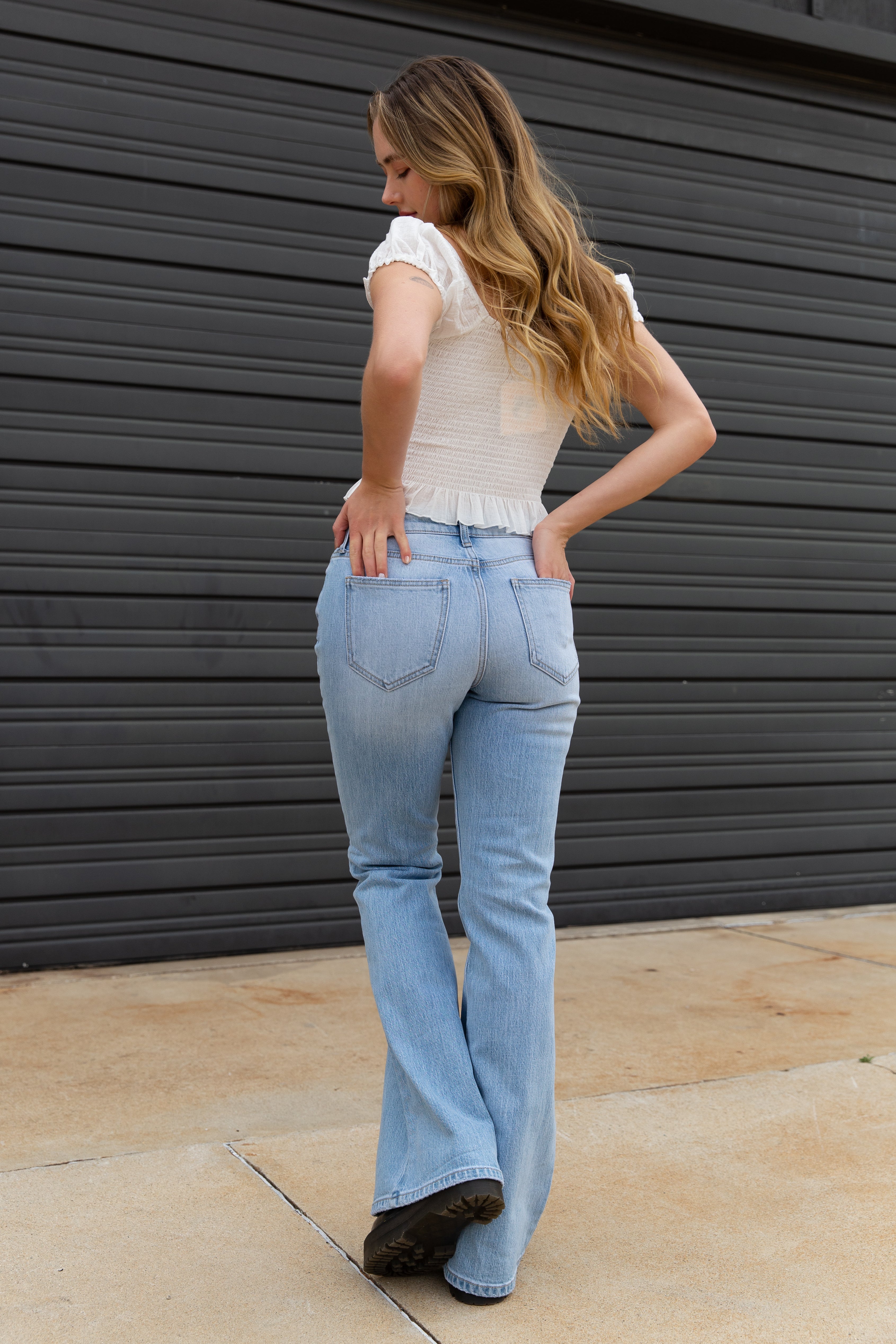 Woman wearing light blue jeans and a white top standing against a dark gray wall.