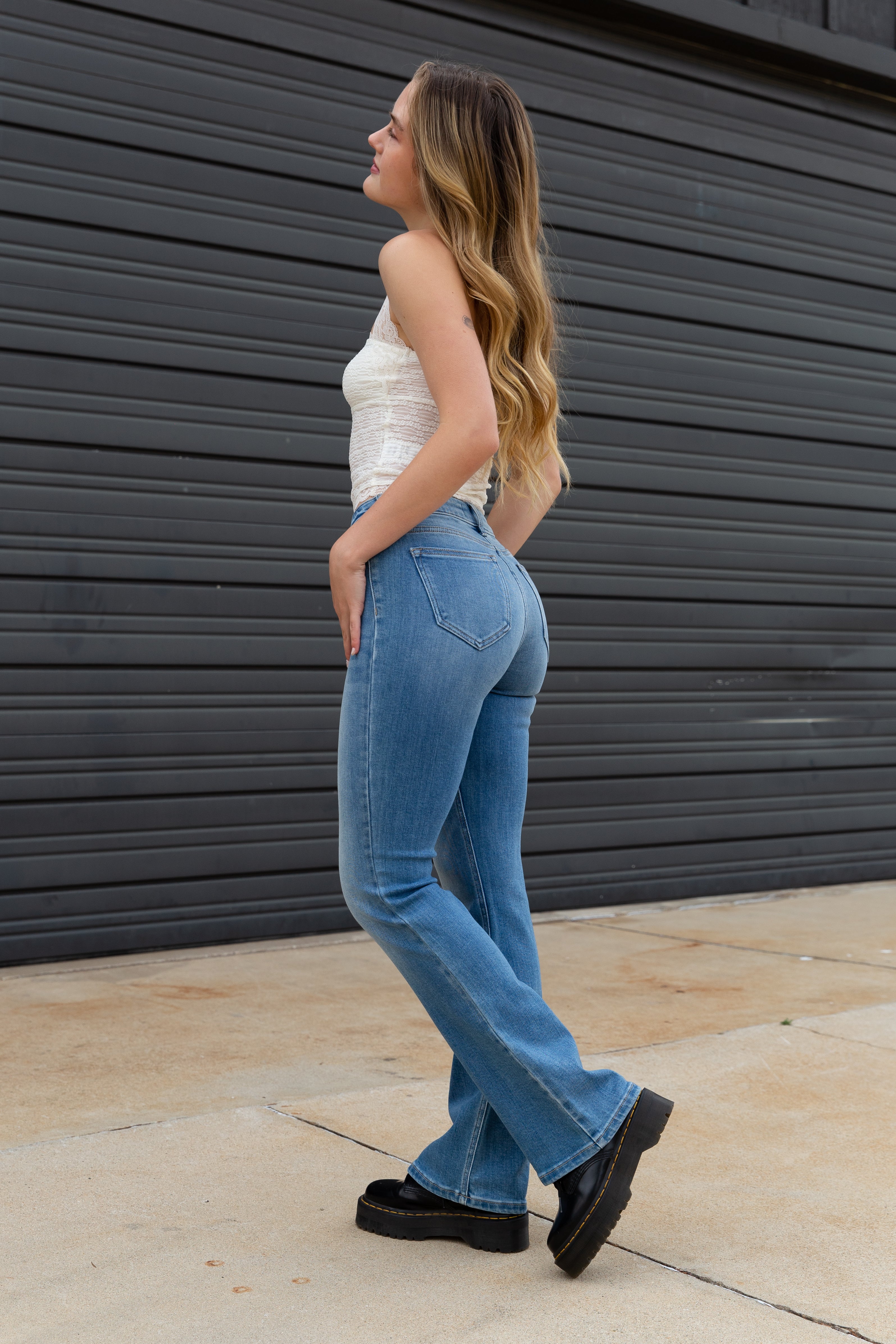 Woman wearing blue jeans and a white top standing against a dark gray wall.
