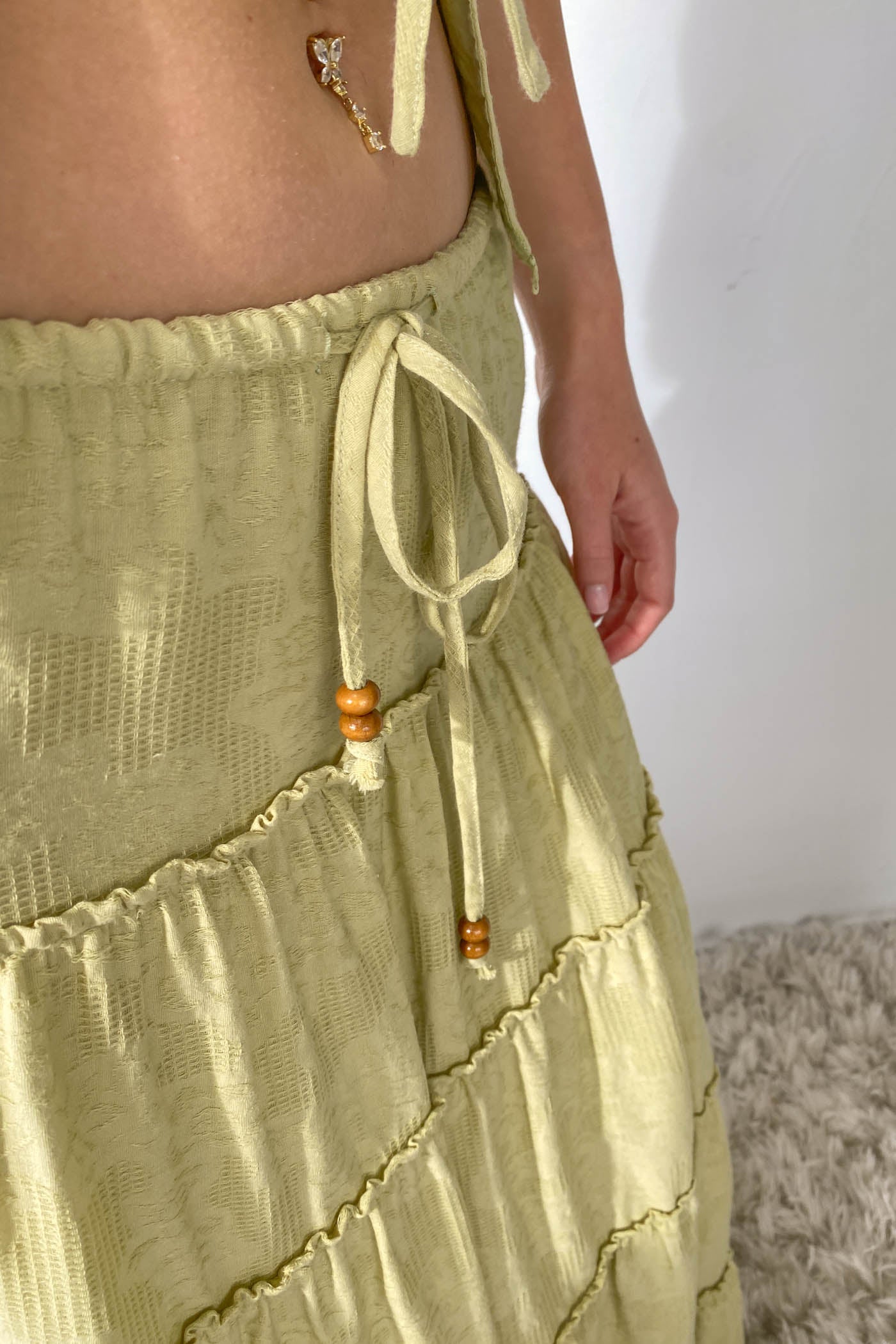 Light green skirt with textured pattern and wooden beads on a neutral background