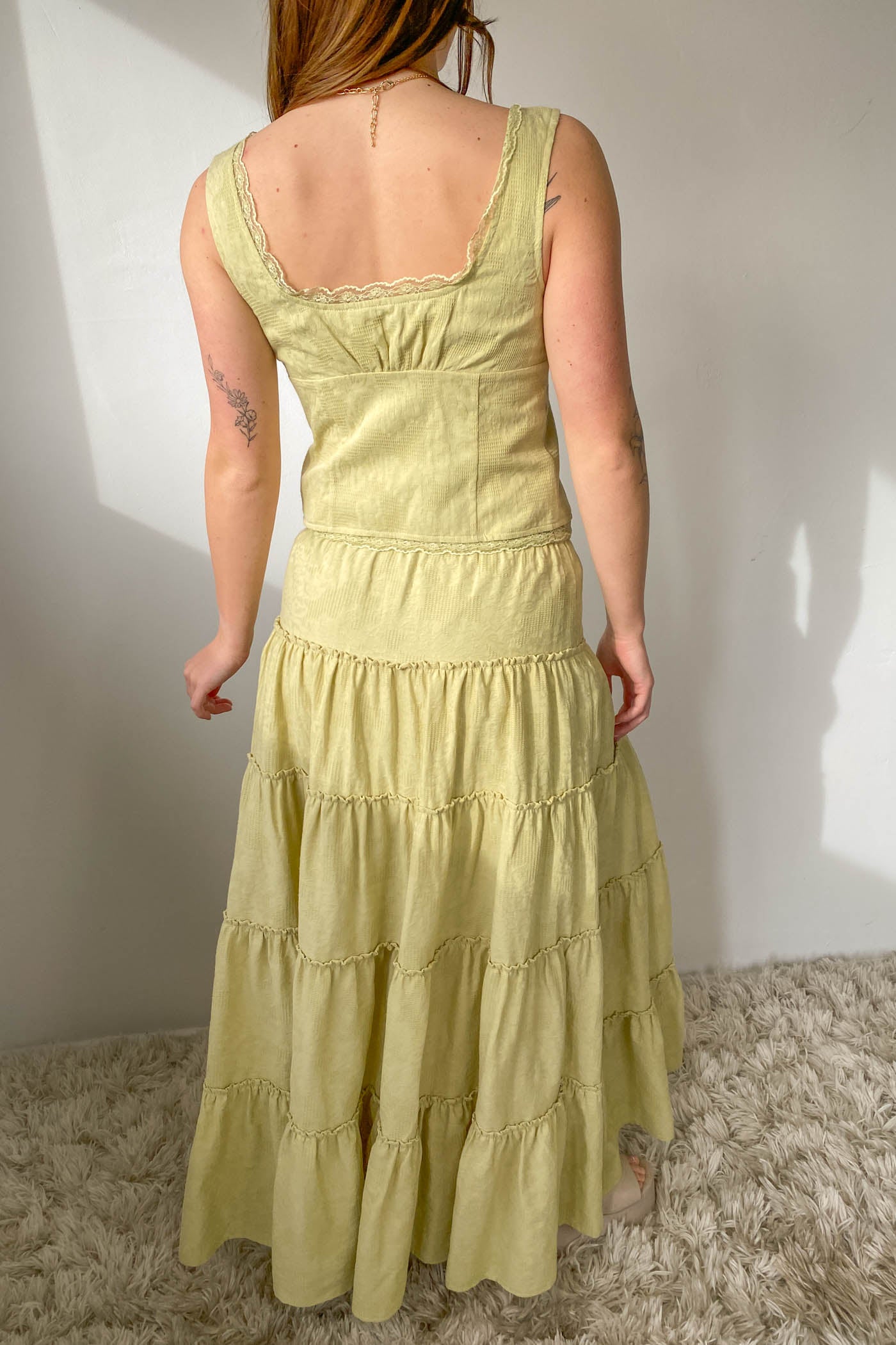 Person wearing a light green tiered dress against a white wall.