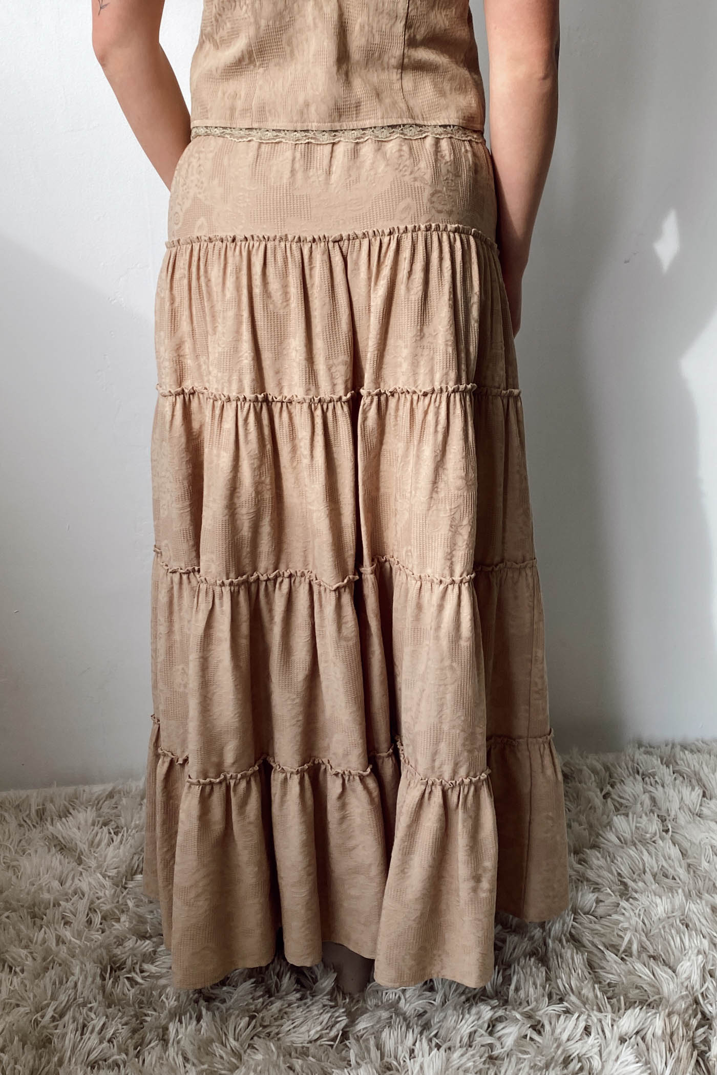 Person wearing a tiered beige dress standing on a fluffy rug with a white wall background
