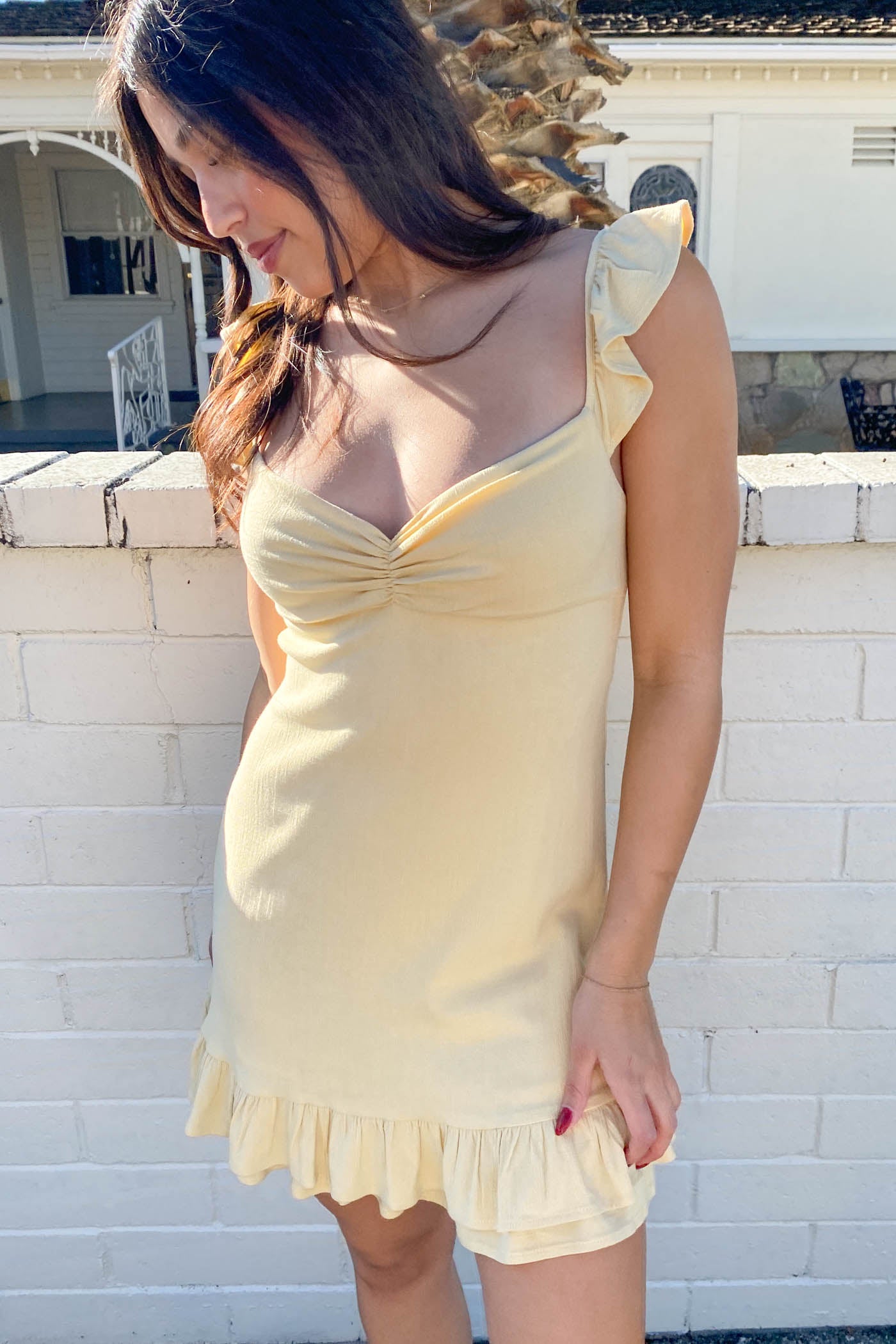 Woman wearing a yellow dress standing against a white brick wall.