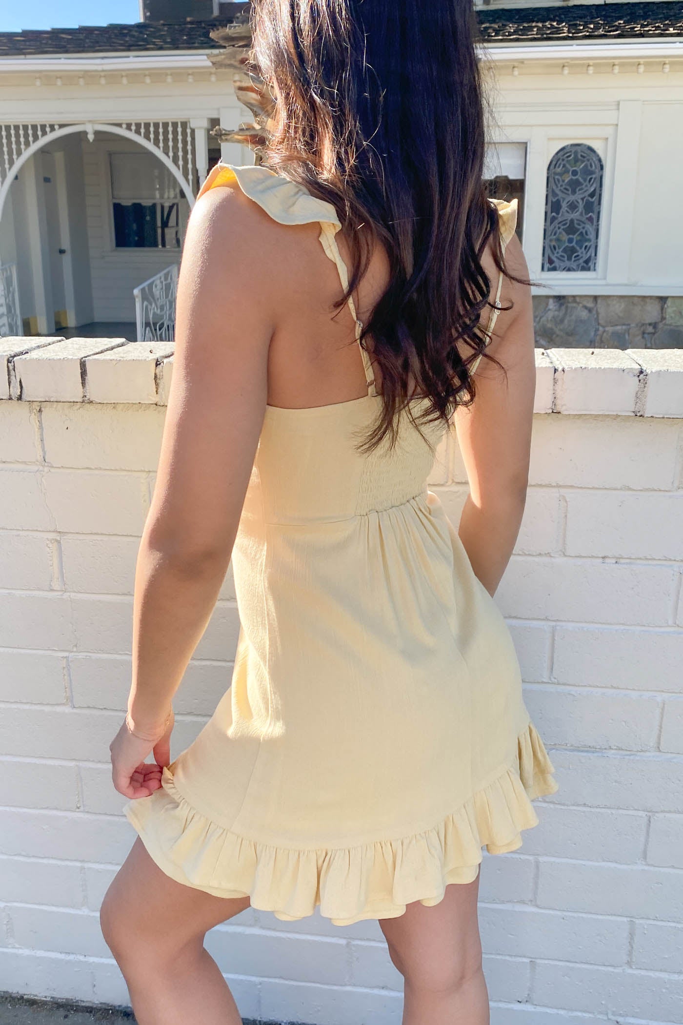 Woman wearing a yellow dress standing against a white brick wall.