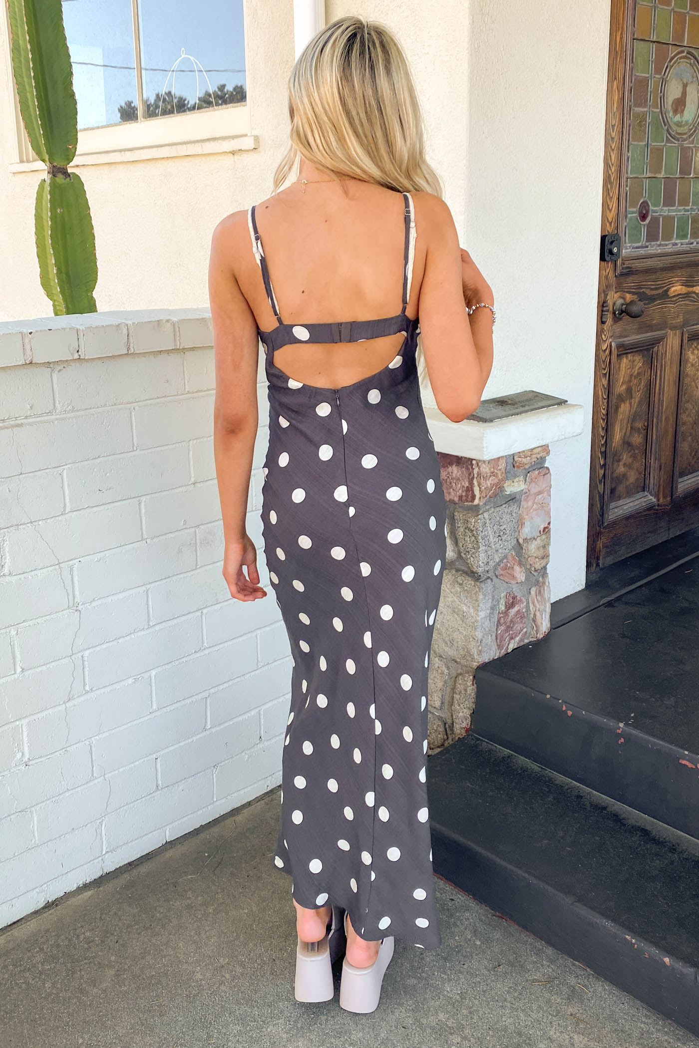 Girl wearing a black Polka Dotted Maxi Dress standing in front of a brick wall. 