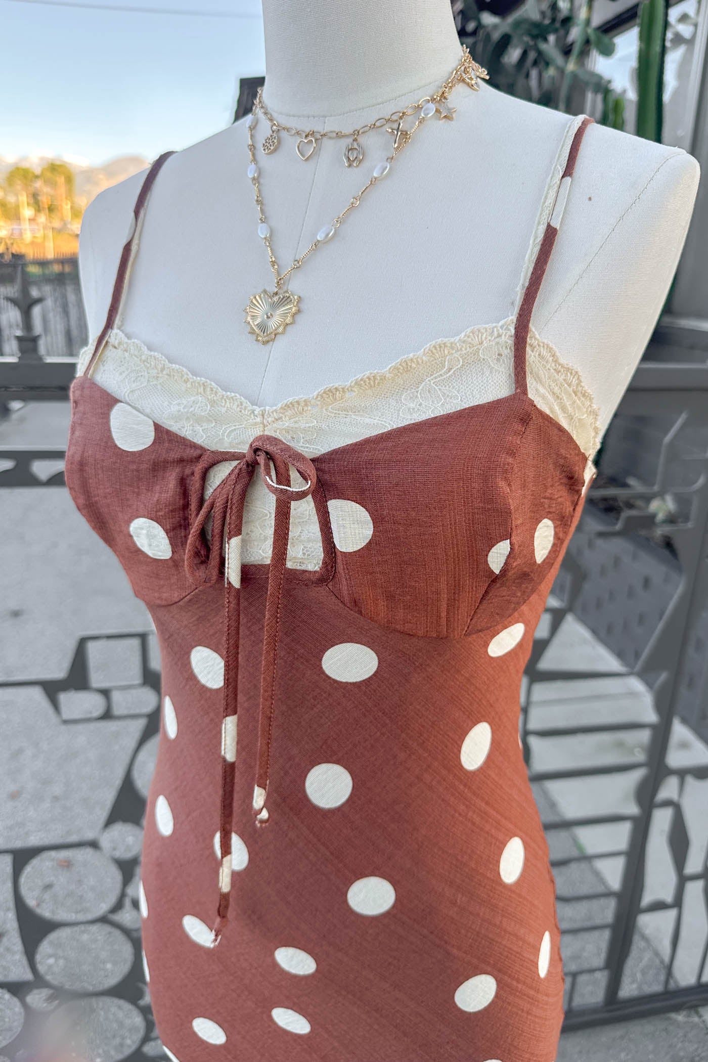 Mannequin wearing a Brown Polka Dotted Maxi Dress standing in front of a fence.