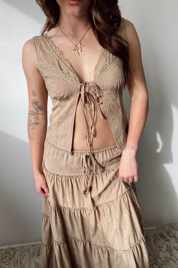 Woman wearing a beige lace-up top and skirt set against a plain background