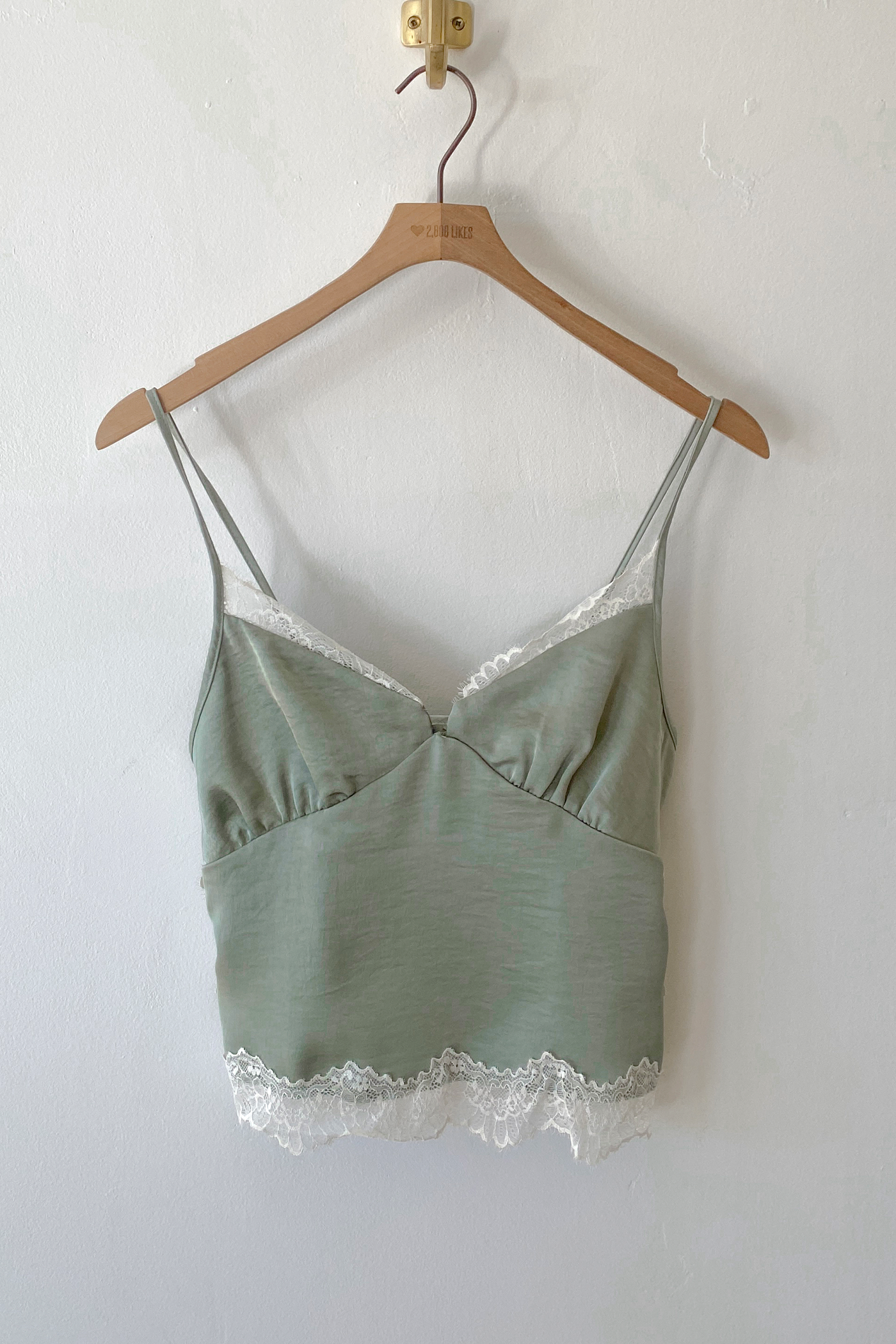Green camisole with lace trim on a wooden hanger against a white wall