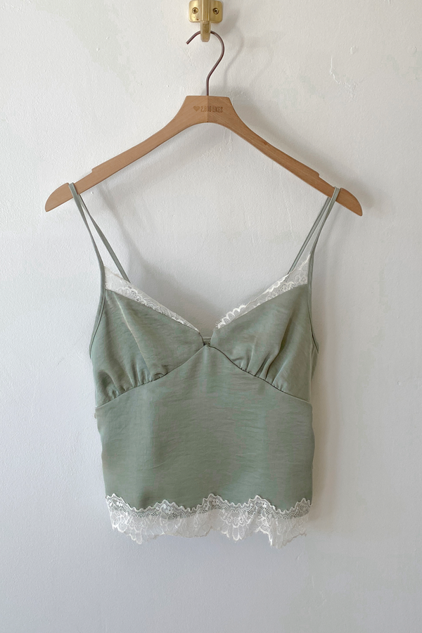 Green camisole with lace trim on a wooden hanger against a white wall