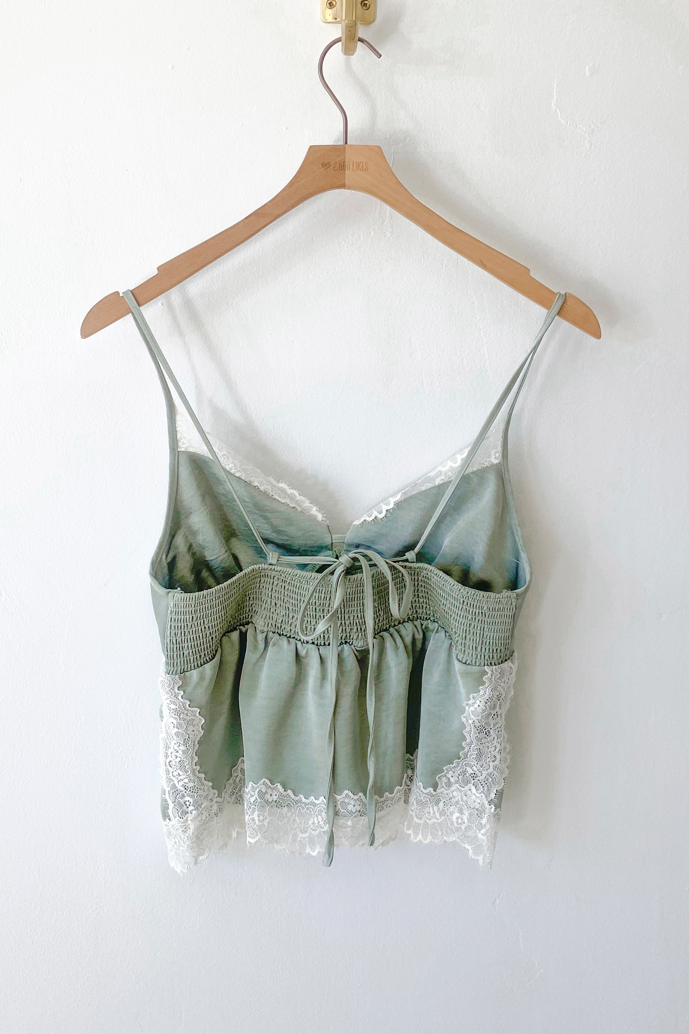 Green lace-trimmed top on a wooden hanger against a white wall