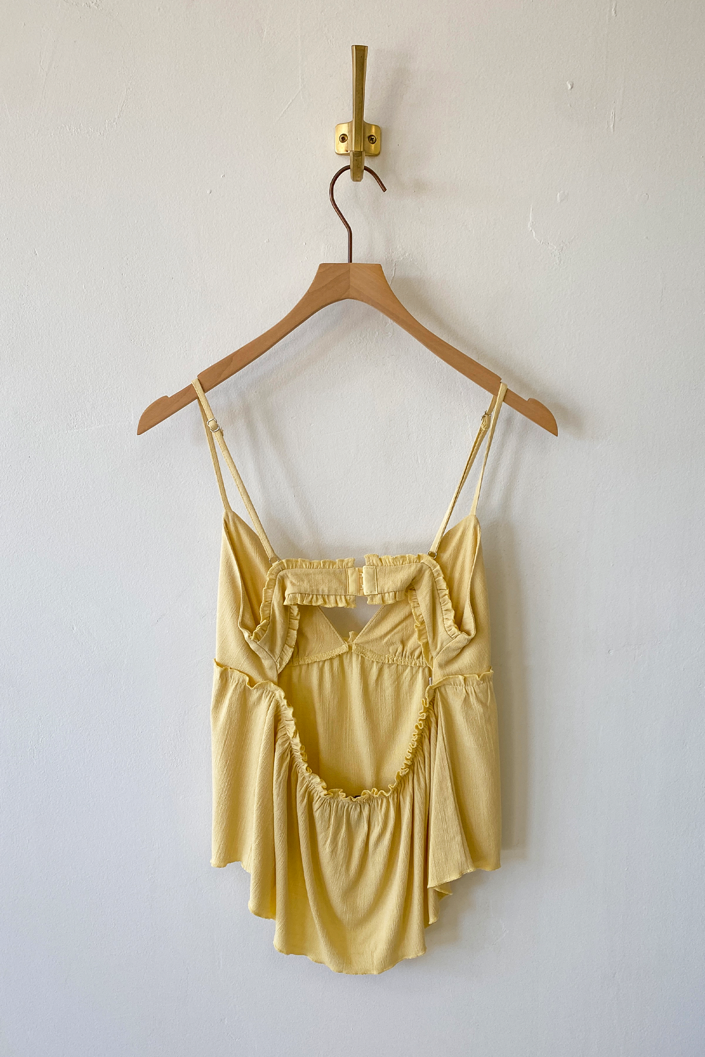 Yellow top on a wooden hanger against a white wall