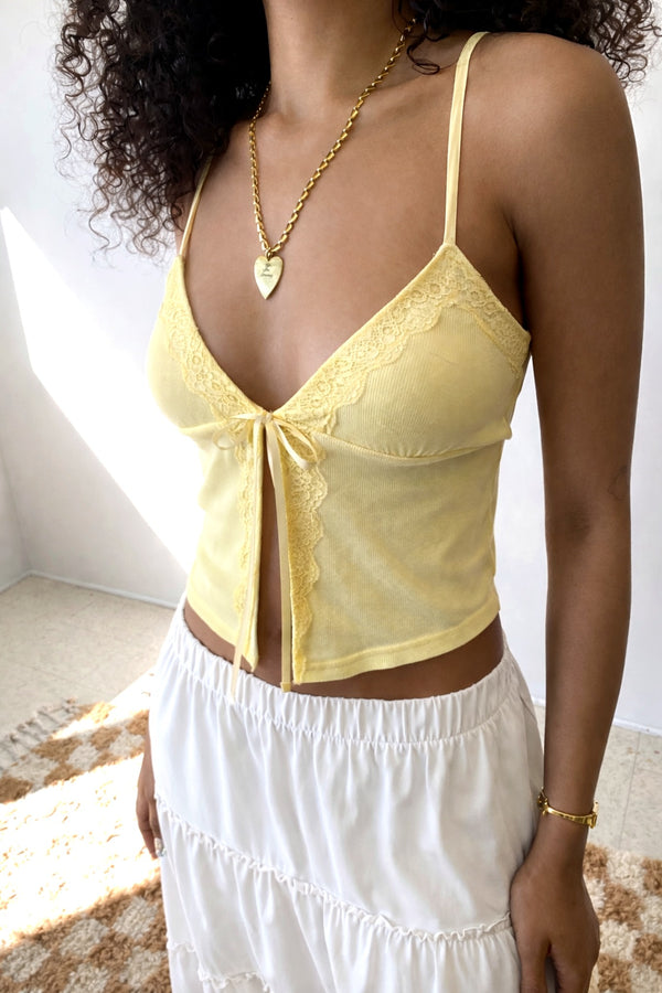 Woman wearing a yellow lace top and white pants indoors.