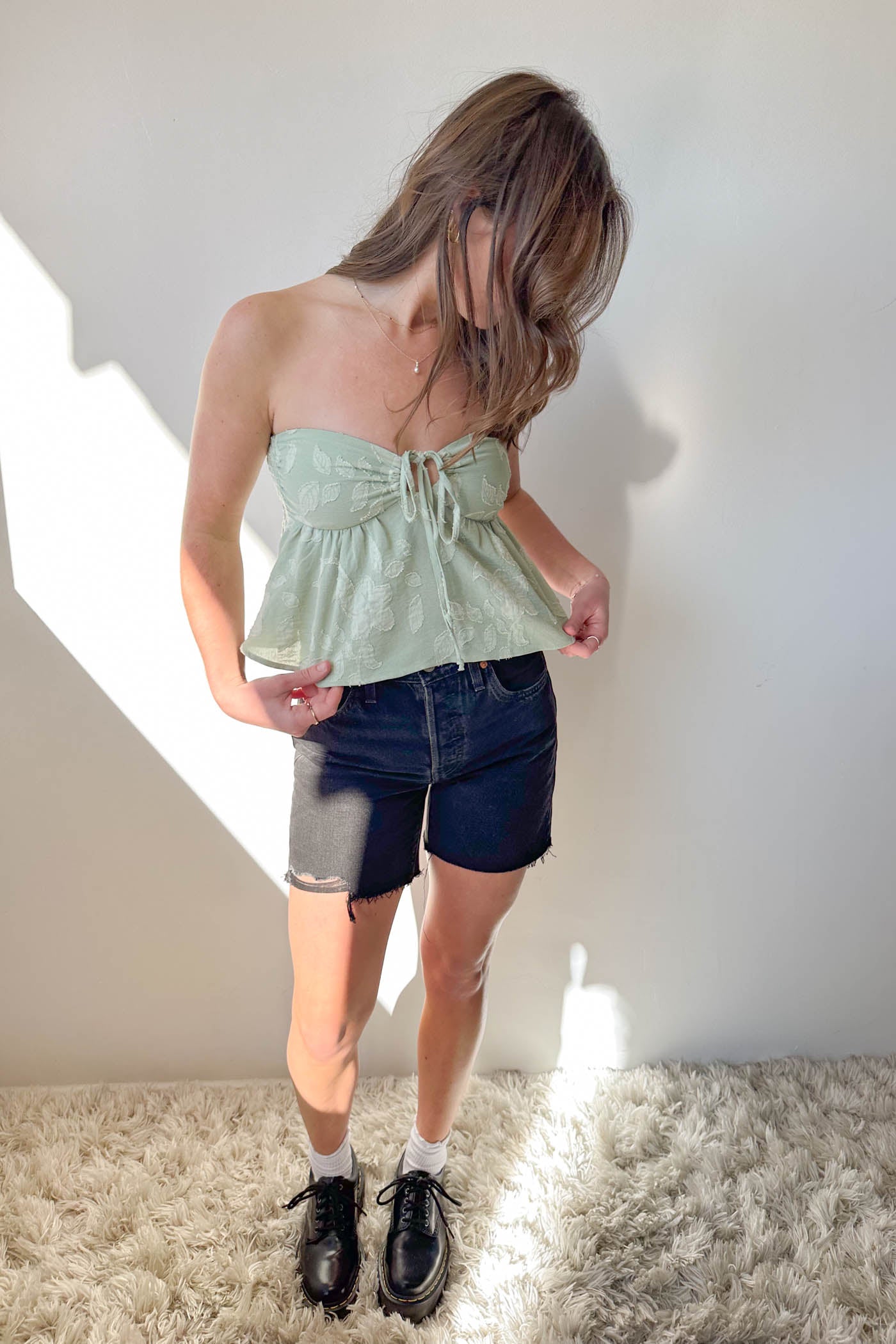 Person wearing a light green strapless top and dark denim shorts on a white background