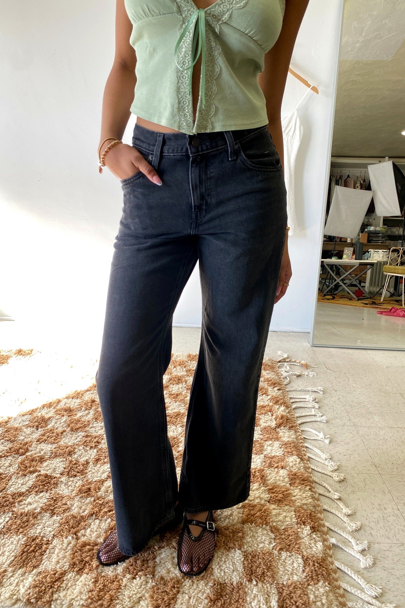 Person wearing a light green top and dark blue jeans standing on a patterned rug.