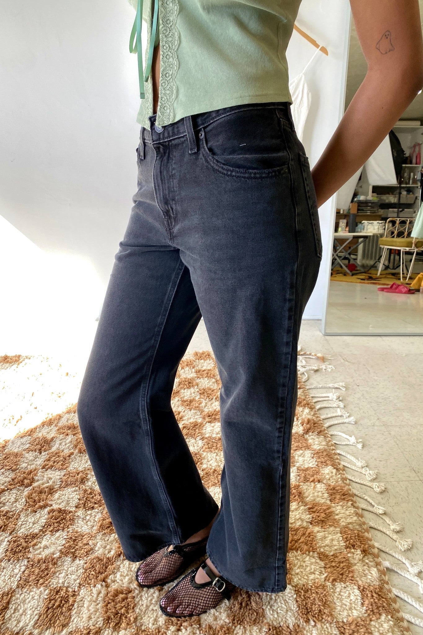 Person wearing dark blue jeans and a light green top on a checkered floor.