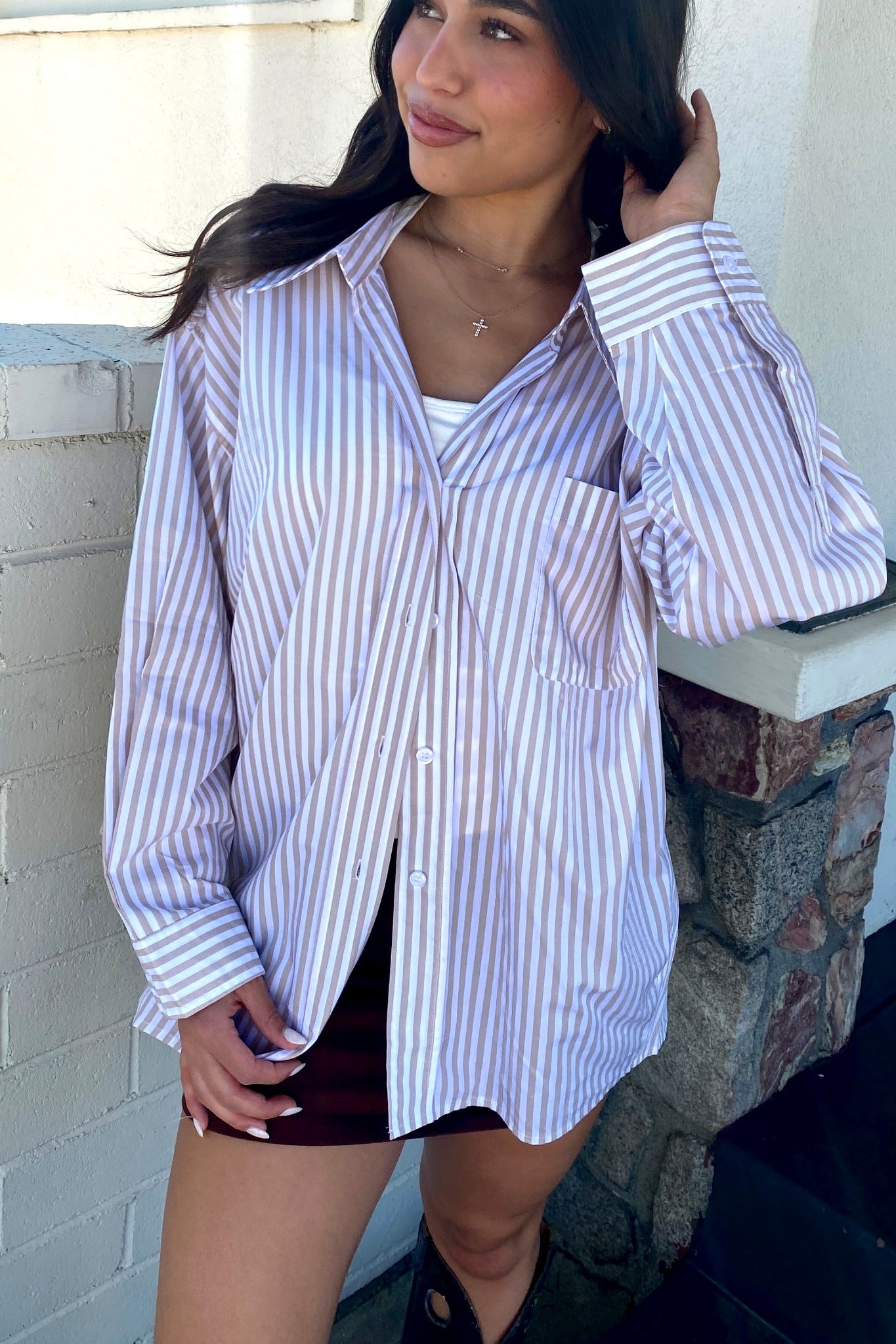 Woman wearing a striped shirt and shorts standing against a brick wall.