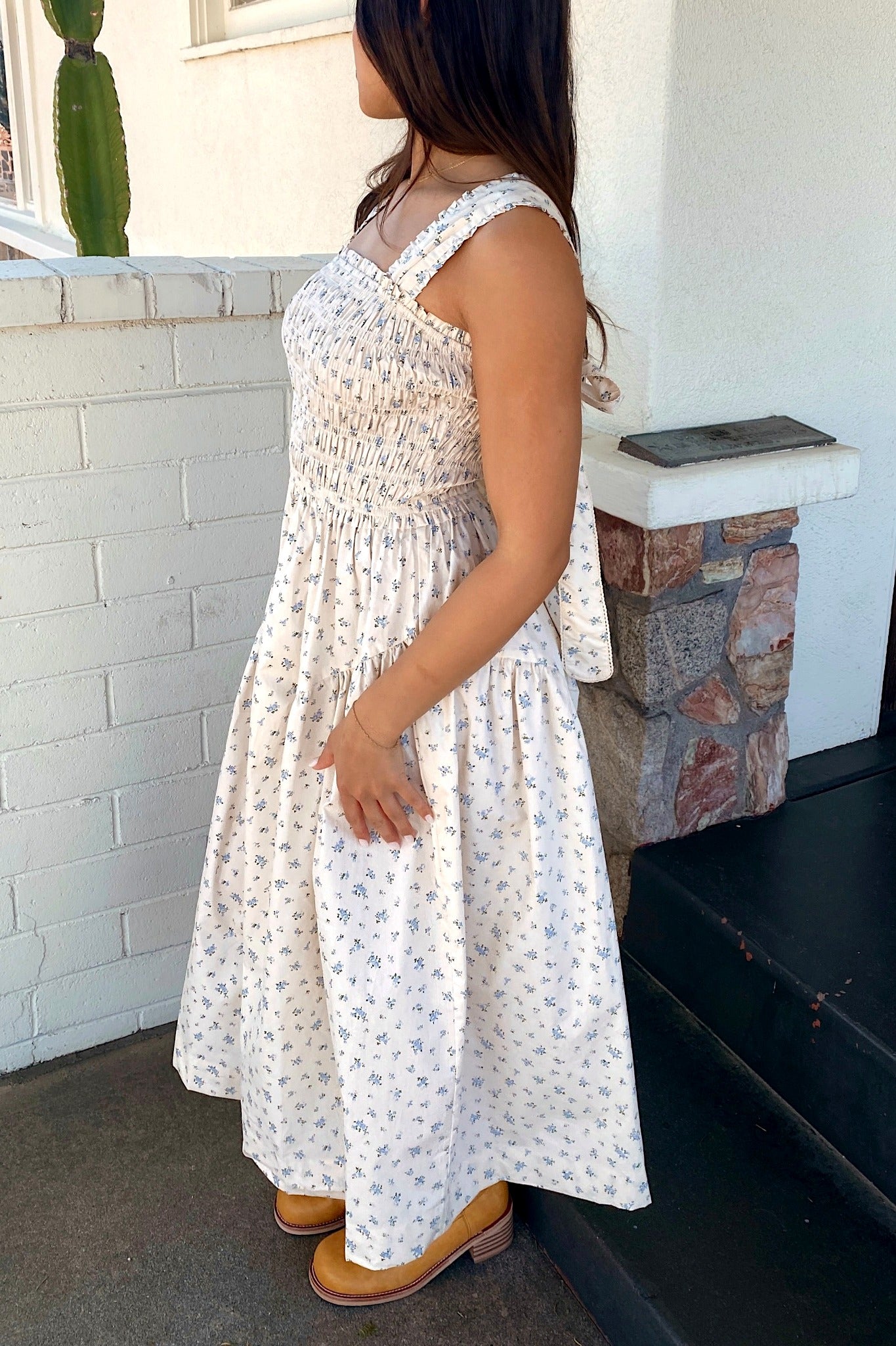Woman in a white floral dress standing in front of a white brick wall with a cactus plant.
