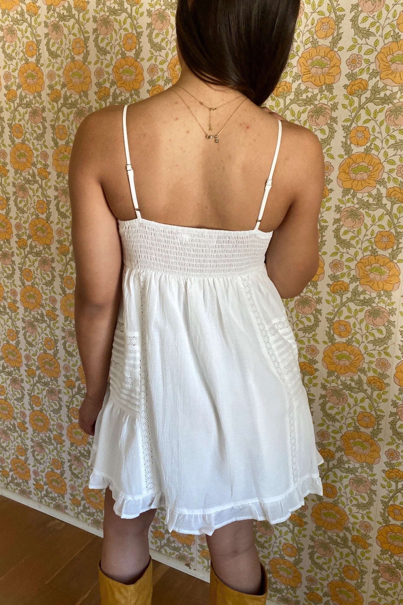 Person wearing a white dress with thin straps against a floral wallpaper background