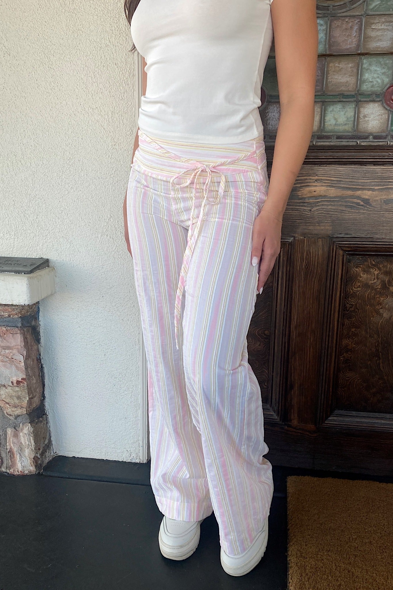 Person wearing a white tank top and pastel striped pants standing indoors.