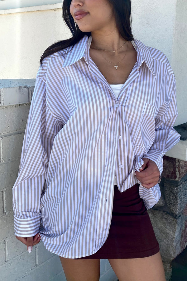 Woman wearing a striped shirt and maroon skirt against a white wall.