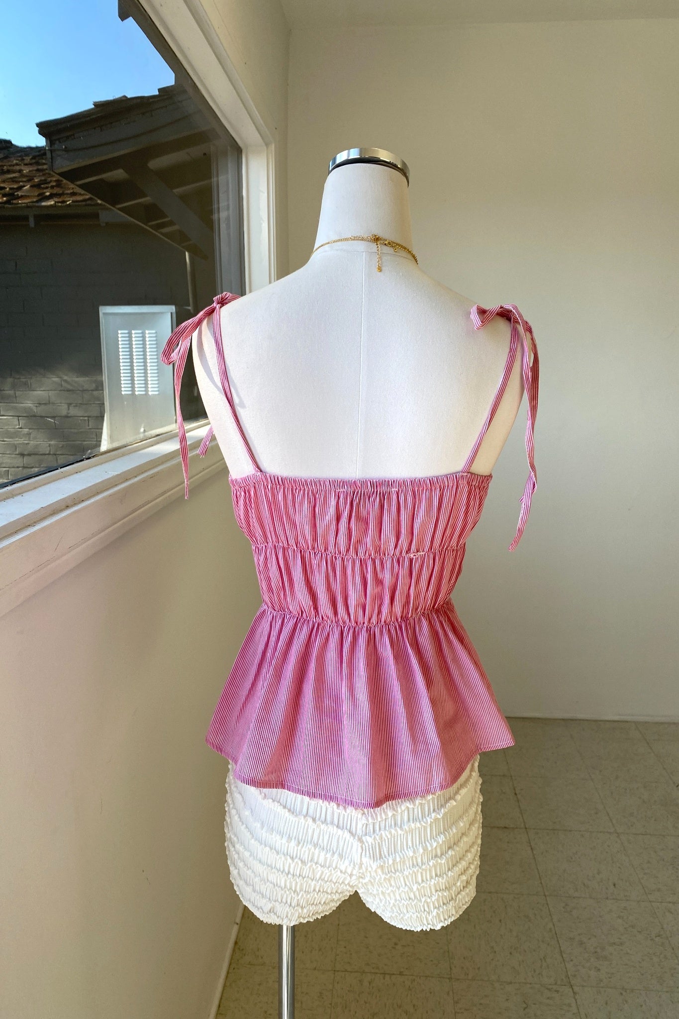 Mannequin wearing a pink top and white shorts in a room with a window.