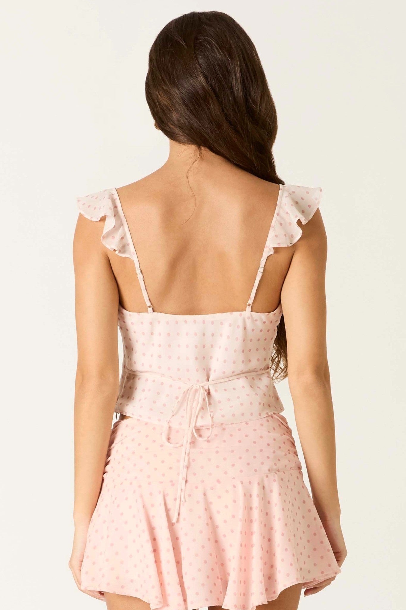 Back view of a woman wearing a light pink dress with lace details on a white background