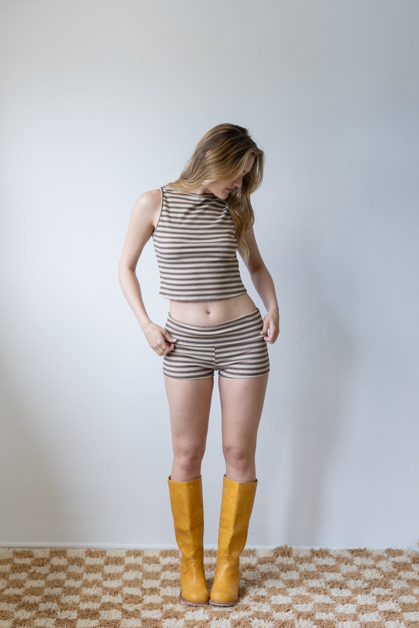 Person wearing a striped tank top and shorts with yellow boots on a plain background