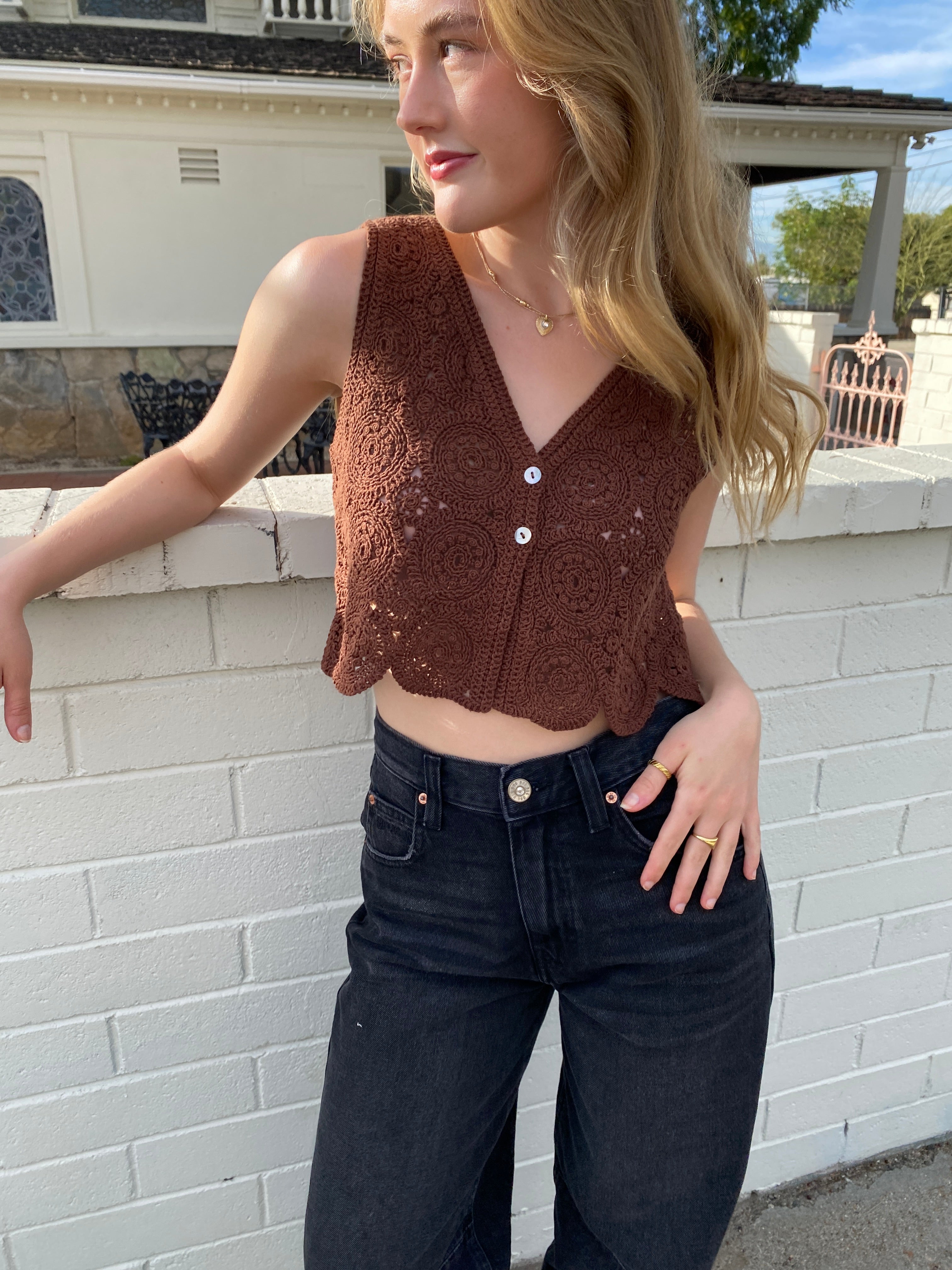 Woman wearing a brown top and dark jeans on a sidewalk.