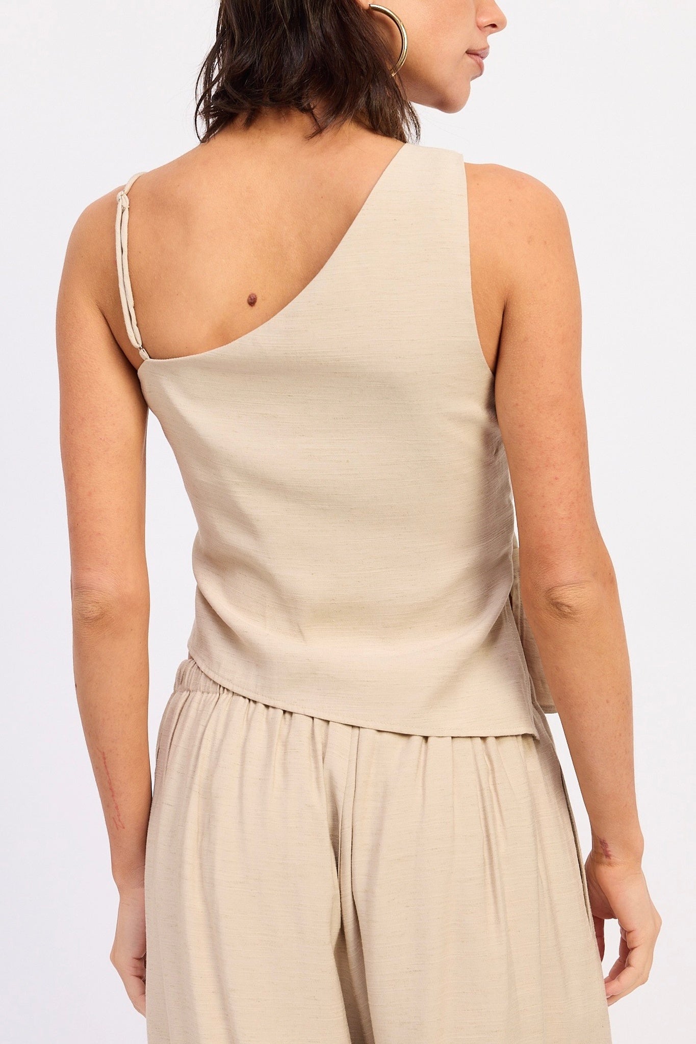 Woman wearing a beige one-shoulder top with a plain background