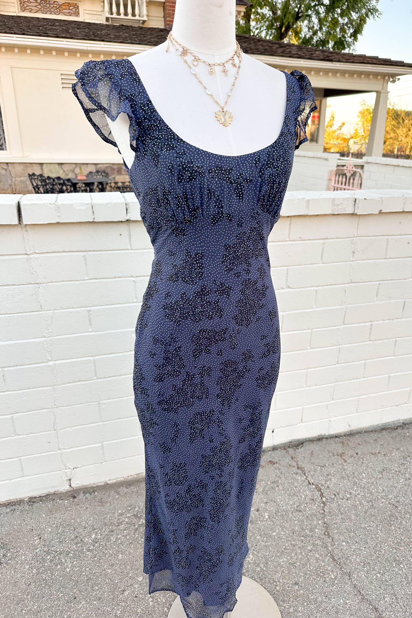 Navy blue lace dress on a mannequin against a white brick wall.