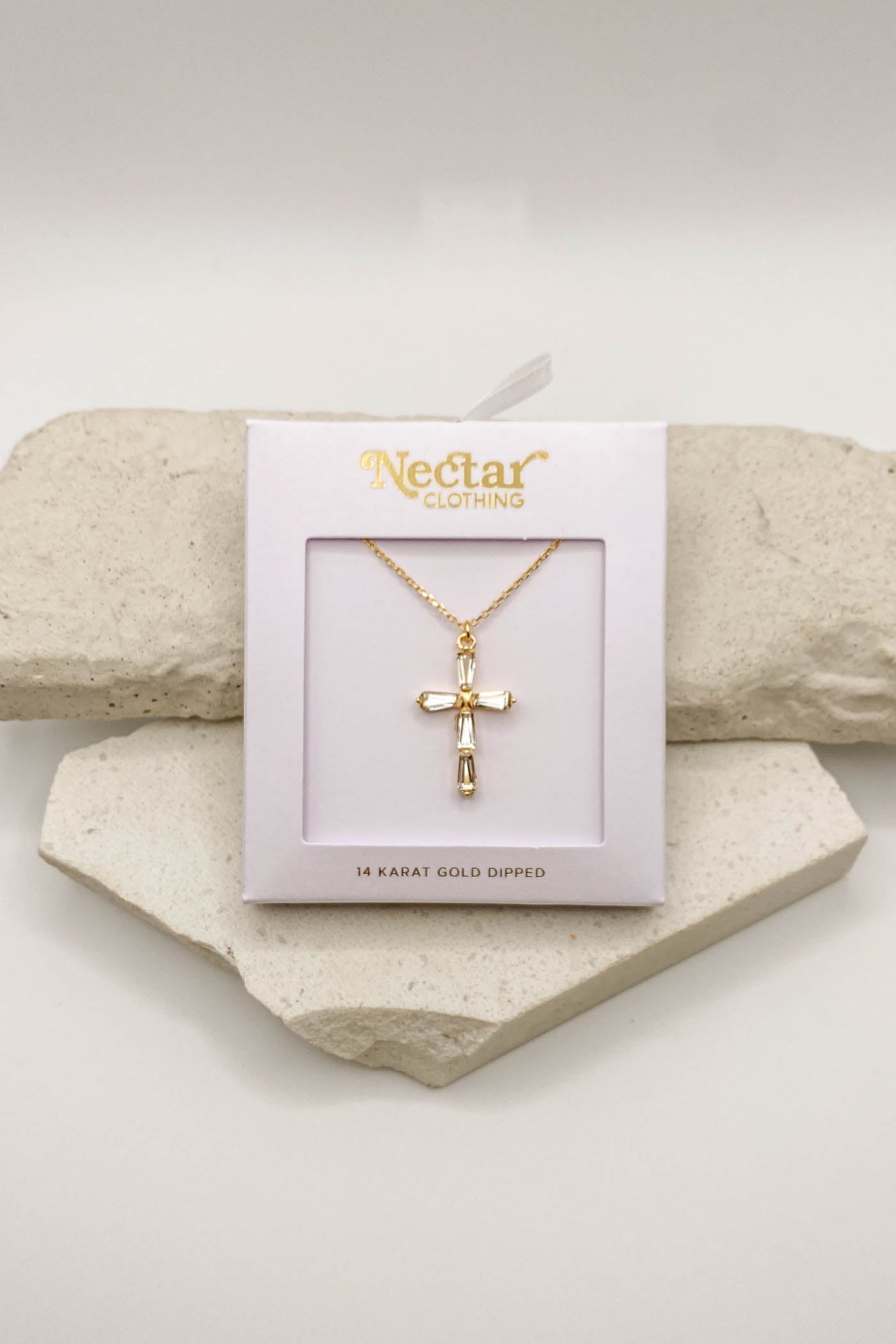 Gold cross necklace on a Nectar Clothing card with a white background