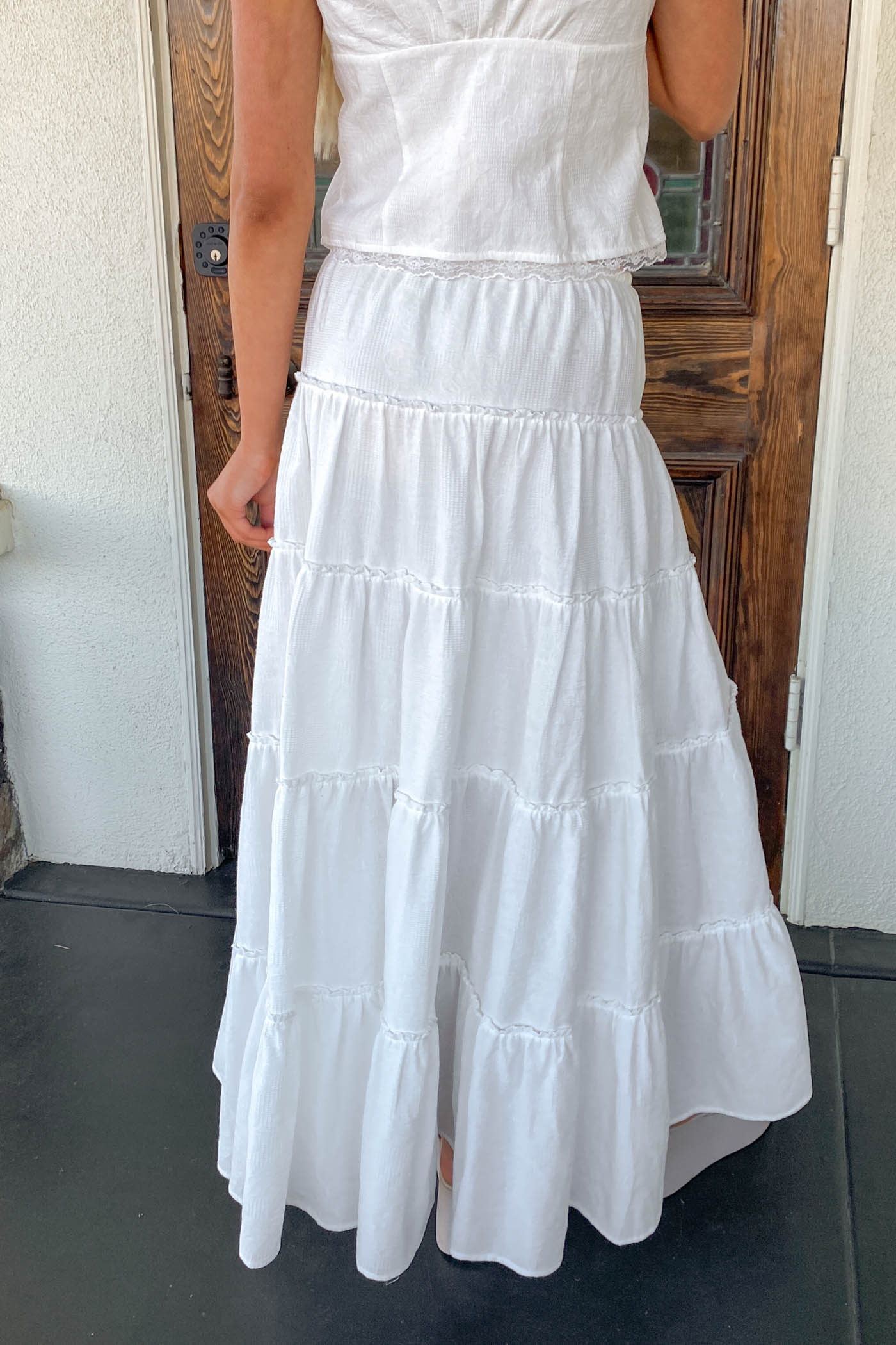 White tiered dress worn by a person standing in front of a wooden door.