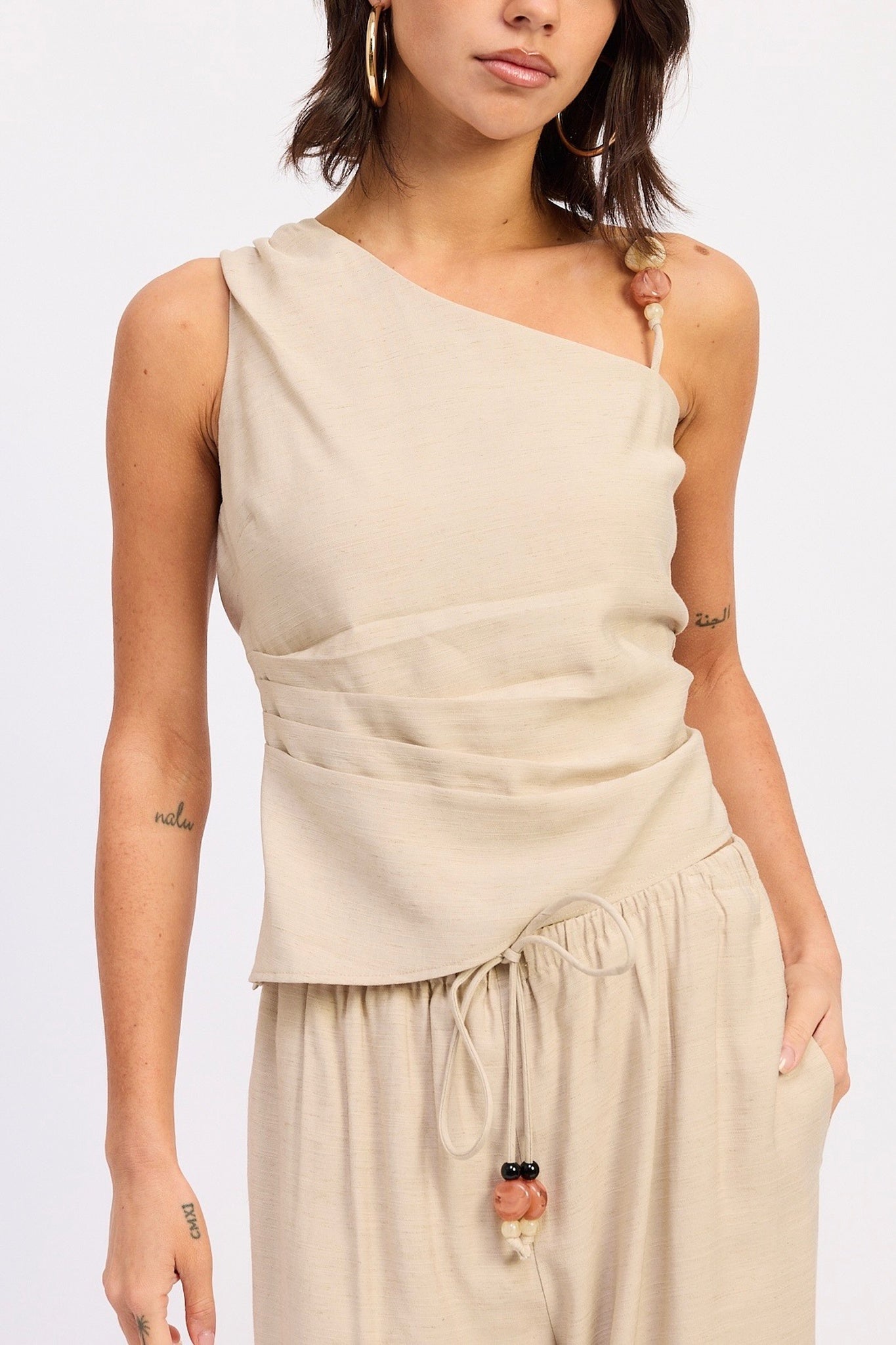 Woman wearing a beige one-shoulder top and matching pants on a white background