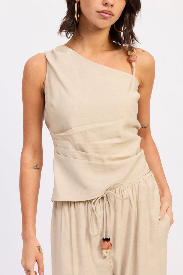 Woman wearing a beige one-shoulder top and matching pants on a white background