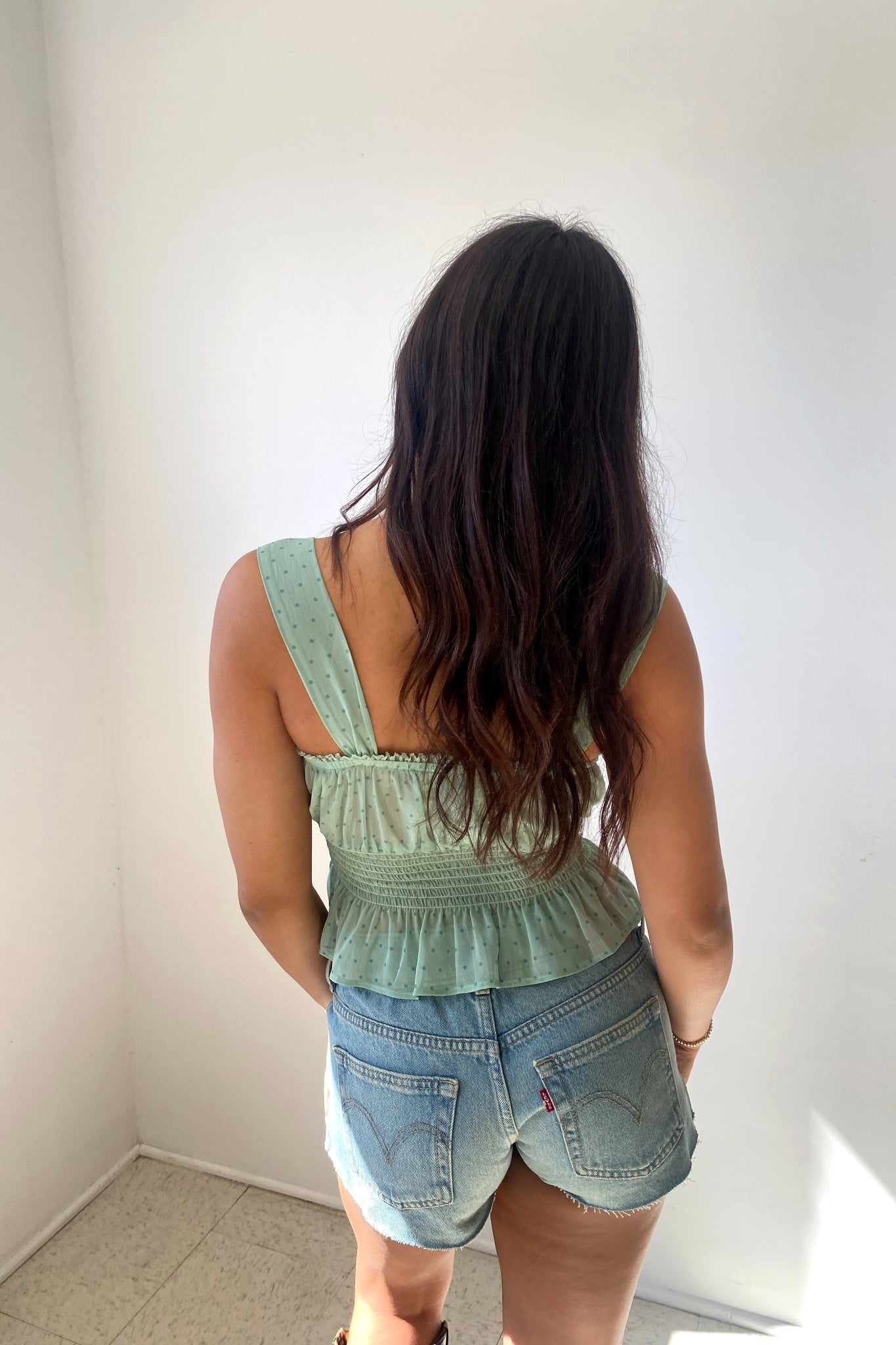 Person wearing a light green top and denim shorts against a white wall.