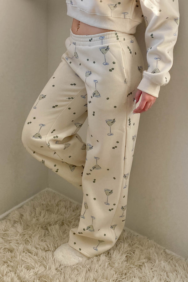 Person wearing a white sweatshirt and patterned pajama pants against a plain wall.