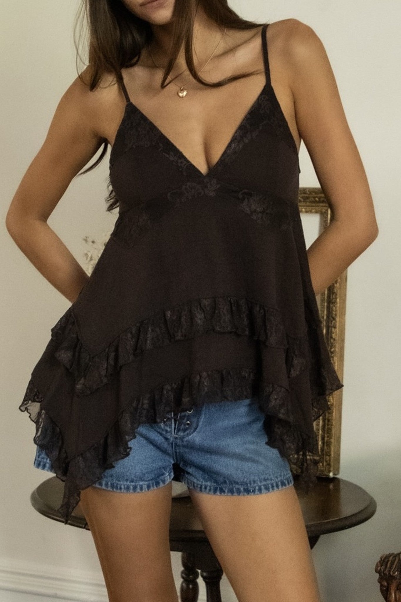Woman wearing a black lace top and denim shorts in a neutral setting